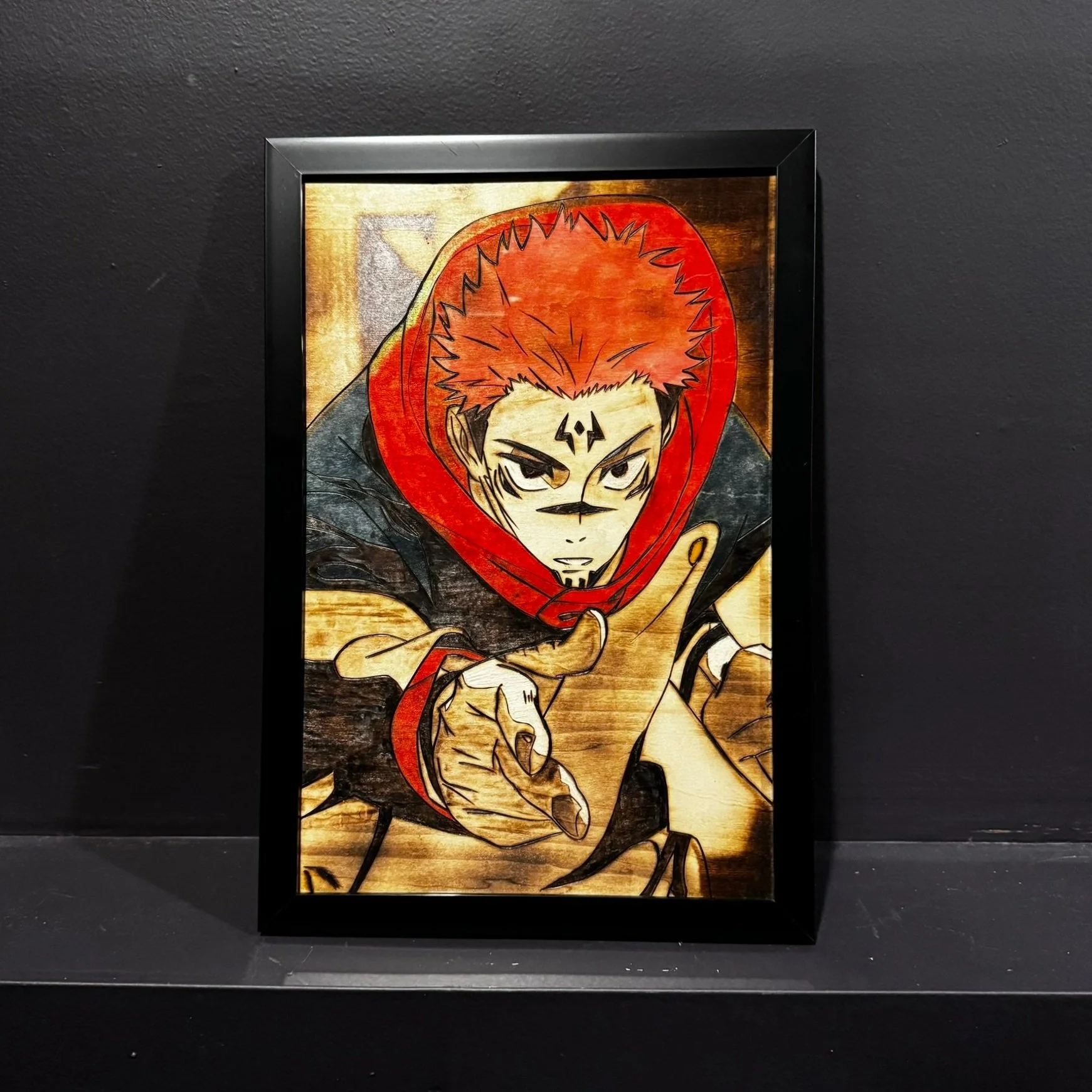 Framed artwork of an anime-style character with red hair, black tattoos, and a red hood, pointing forward with an intense expression.