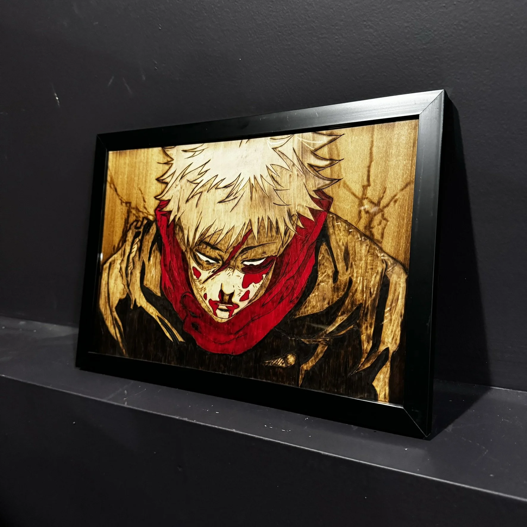 Framed artwork of a person with white hair and blood on their face, wearing a red scarf, looking downward, set against a textured, wooden background.