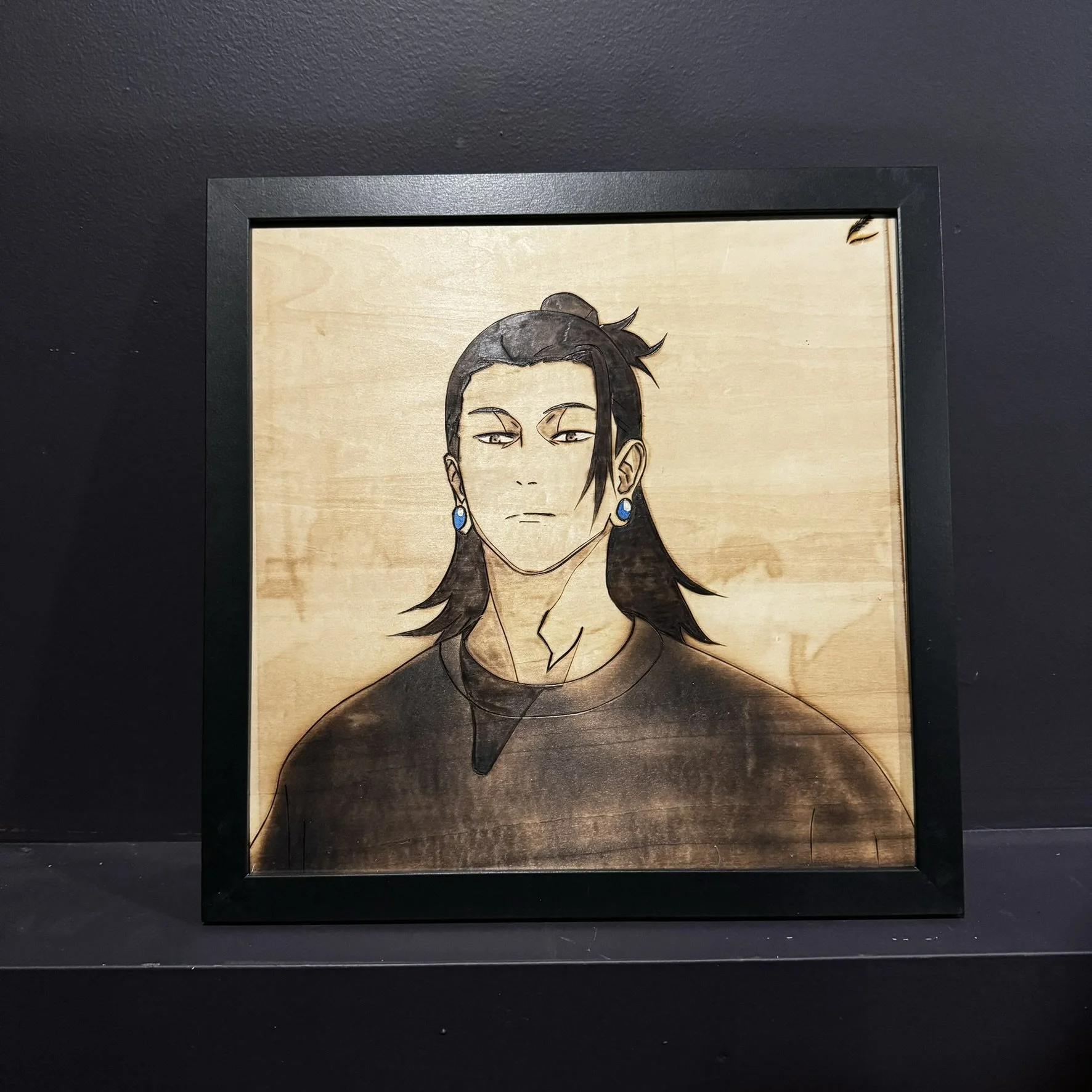 Painting of a male character with long black hair, wearing earrings, and a serious expression, on a wooden background