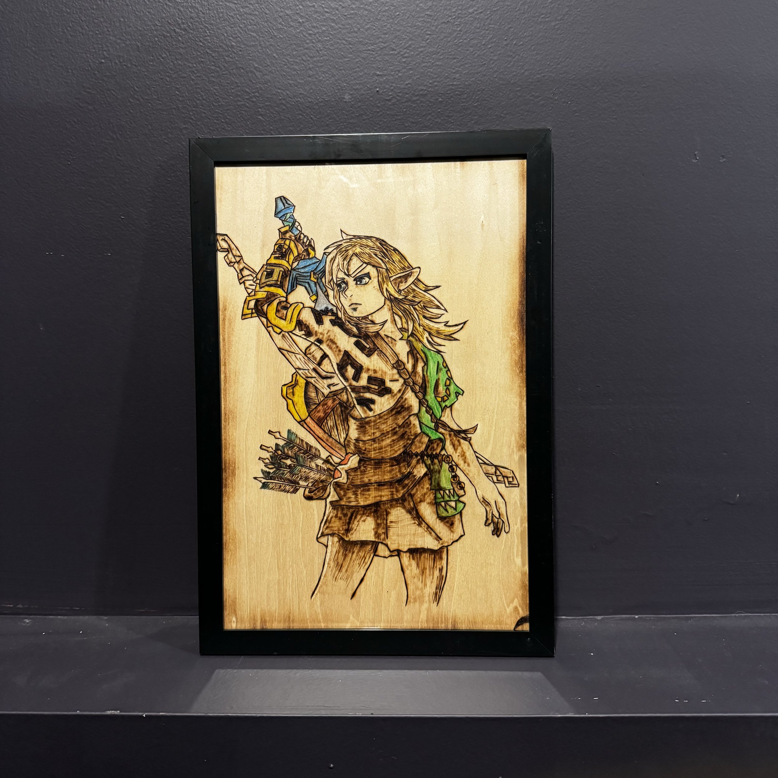 Framed artwork of a video game character holding a sword with a bow and quiver of arrows, depicted on a wooden panel.