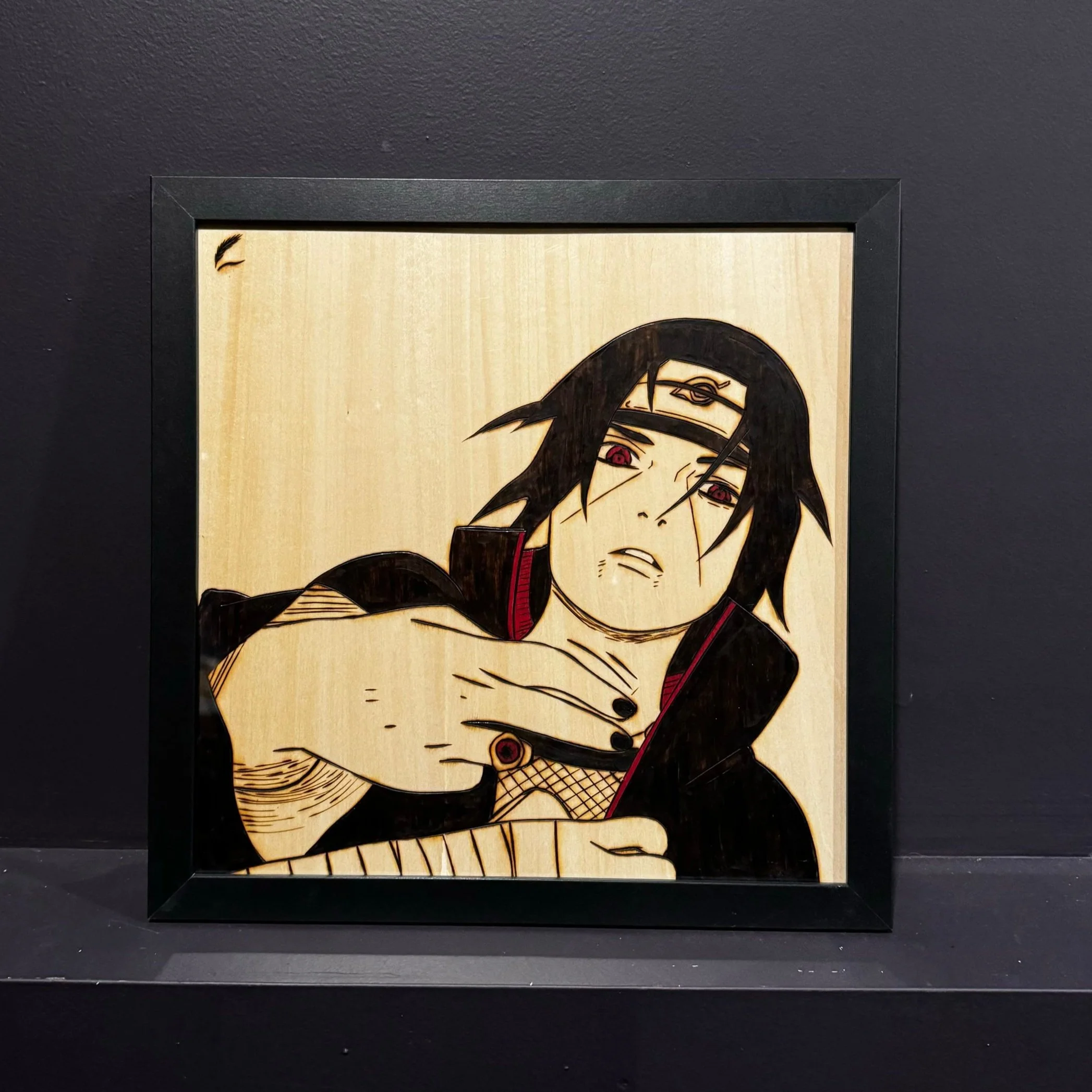 Wooden framed artwork of a male anime character with black hair, red eyes, and a headband, wearing a black jacket with red accents, holding his hand to his chest.