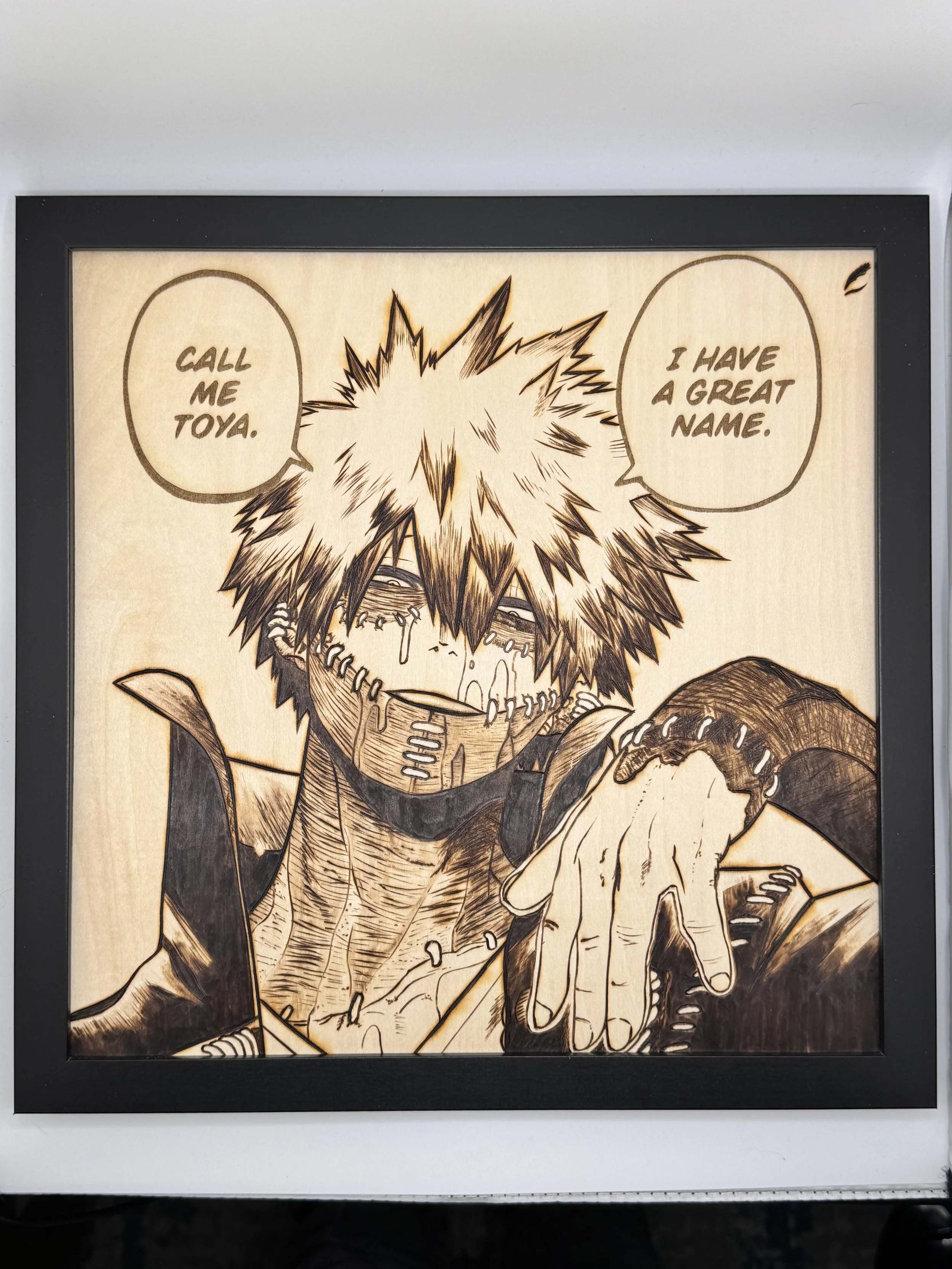 A framed artwork of a manga-style character with spiky hair, tears, and a stitched face, pointing with one hand. The character has speech bubbles stating, "Call me Toya" and "I have a great name."