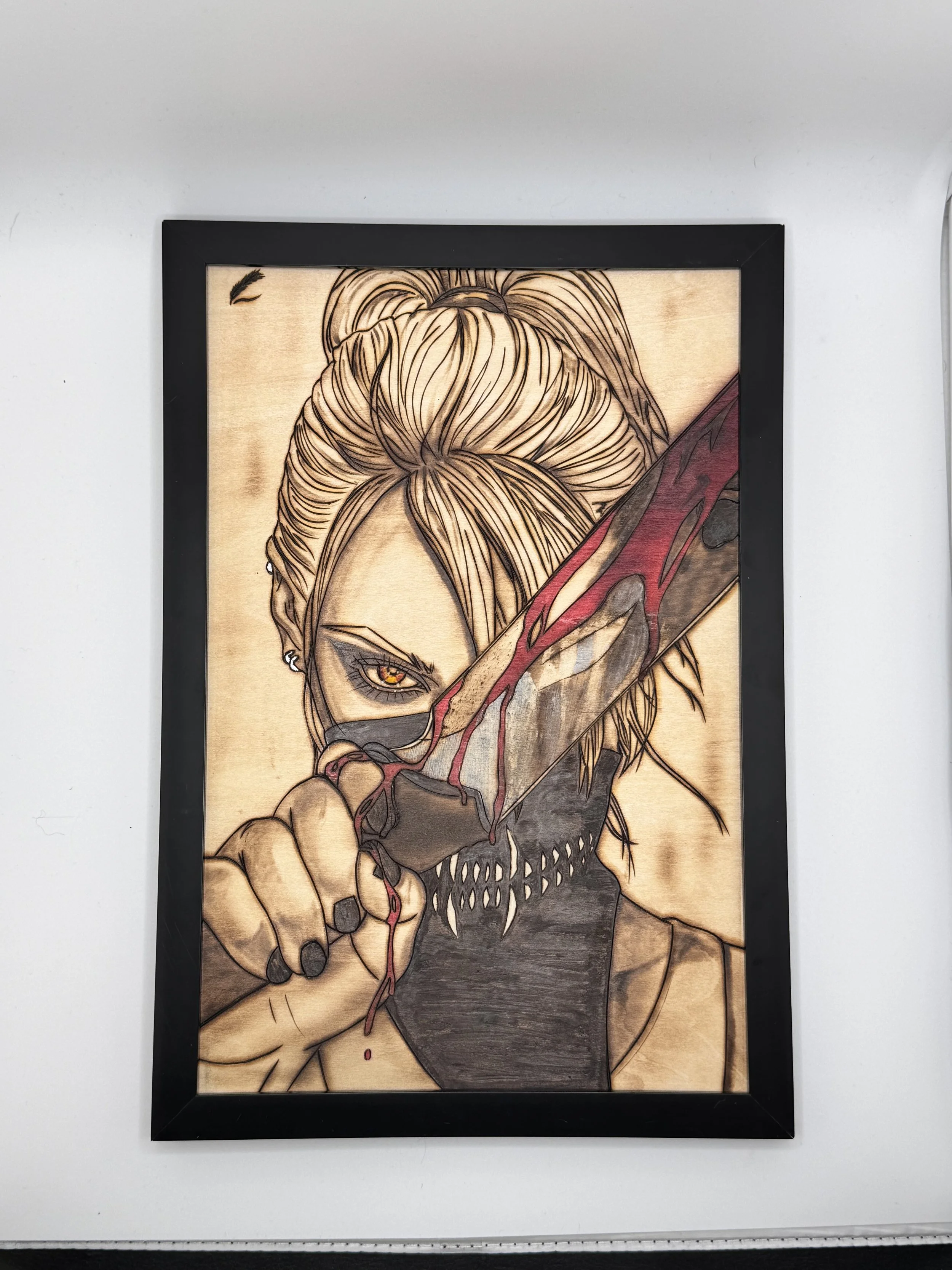 A framed artwork of a woman with blonde hair in a bun, holding a bloodied knife with a skull-like face at the handle, her face partially covered by the knife, with intense eyes and a dark background.