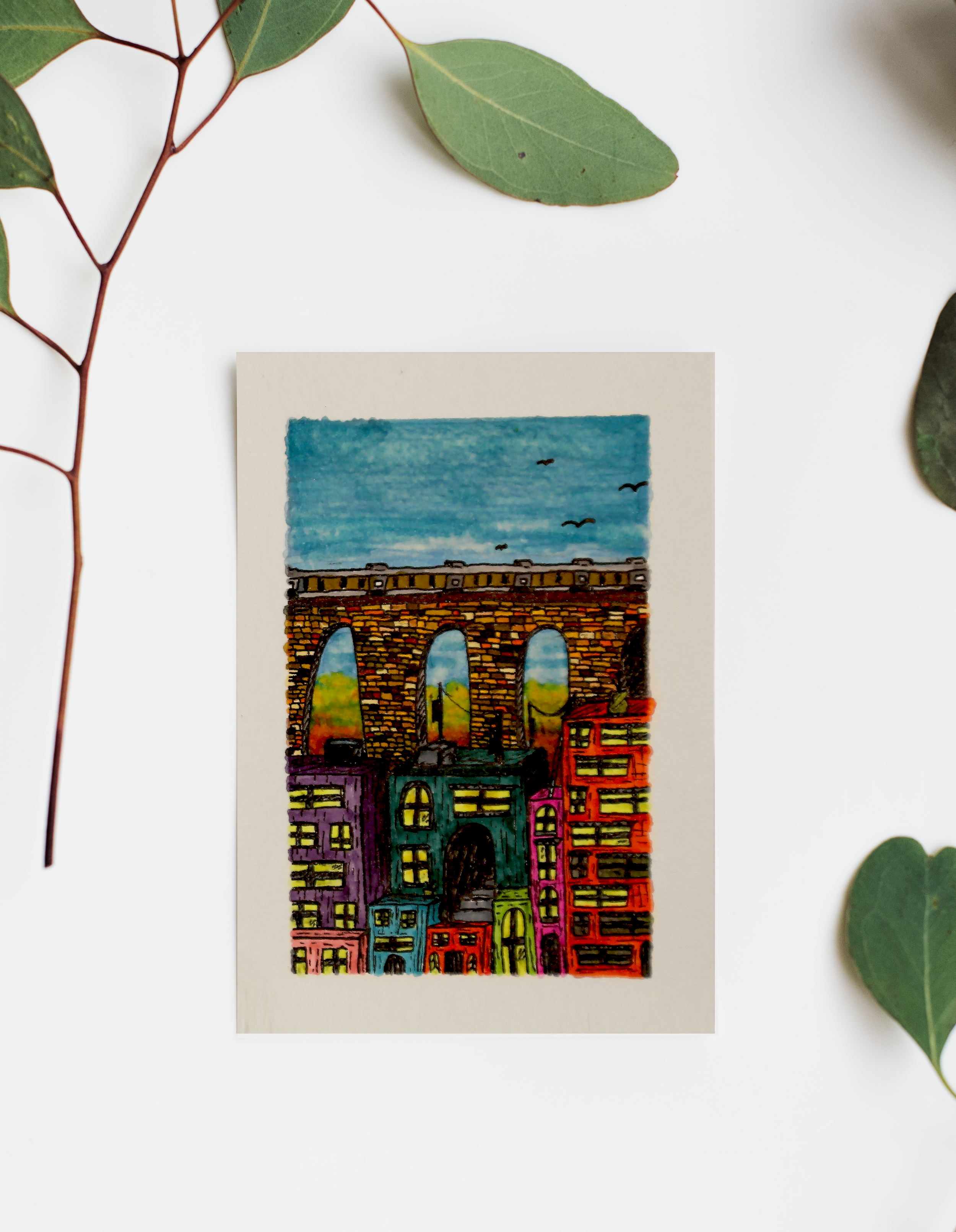 Bridge Scene by Rix – colorful hand-drawn cityscape artwork featuring a stone bridge with arches above bright buildings.