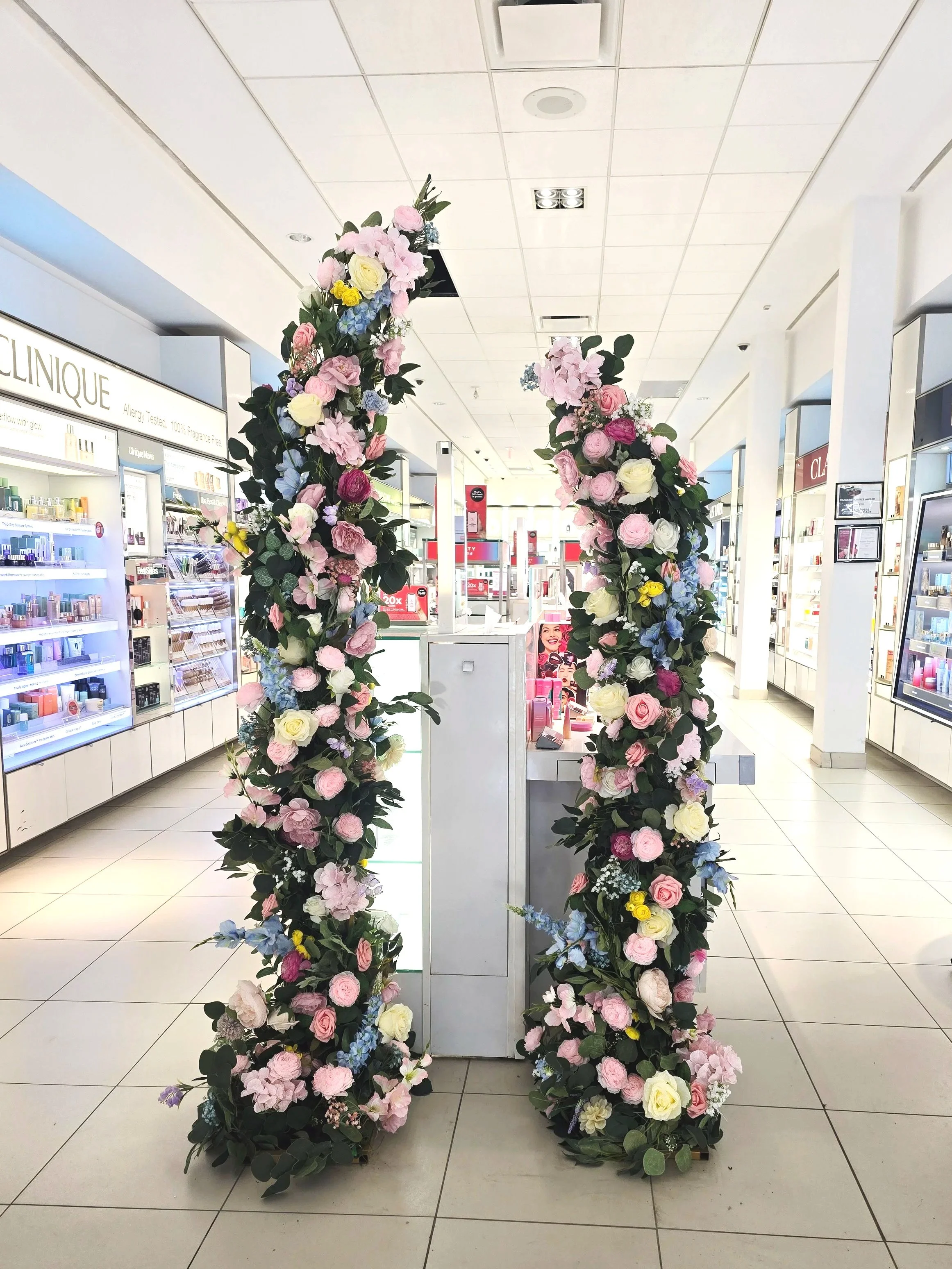 Flower arch made of pink, white, purple, and yellow flowers with green leaves inside a store aisle.