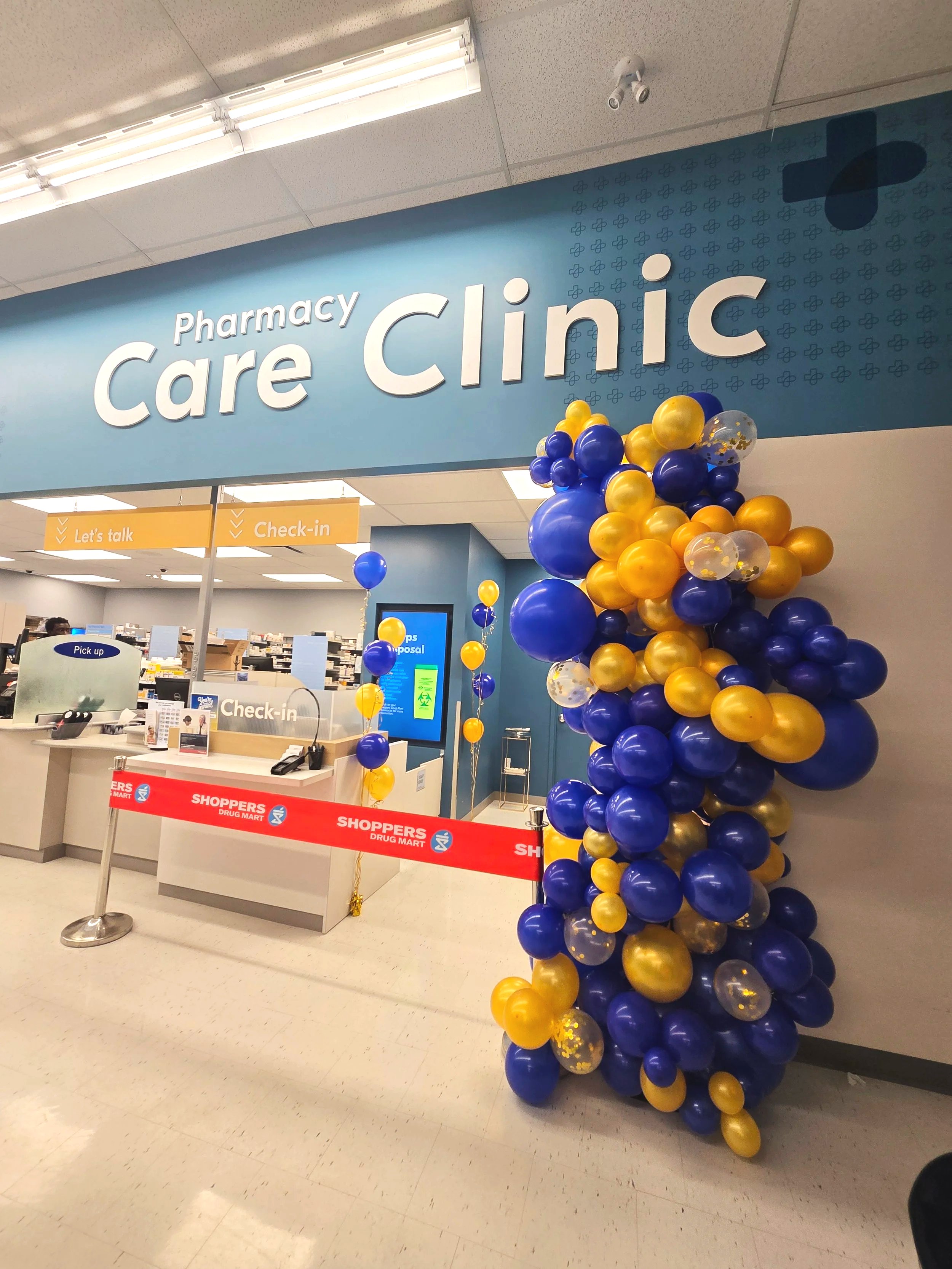 Decorated balloon column in yellow and blue at the entrance to a pharmacy and care clinic.