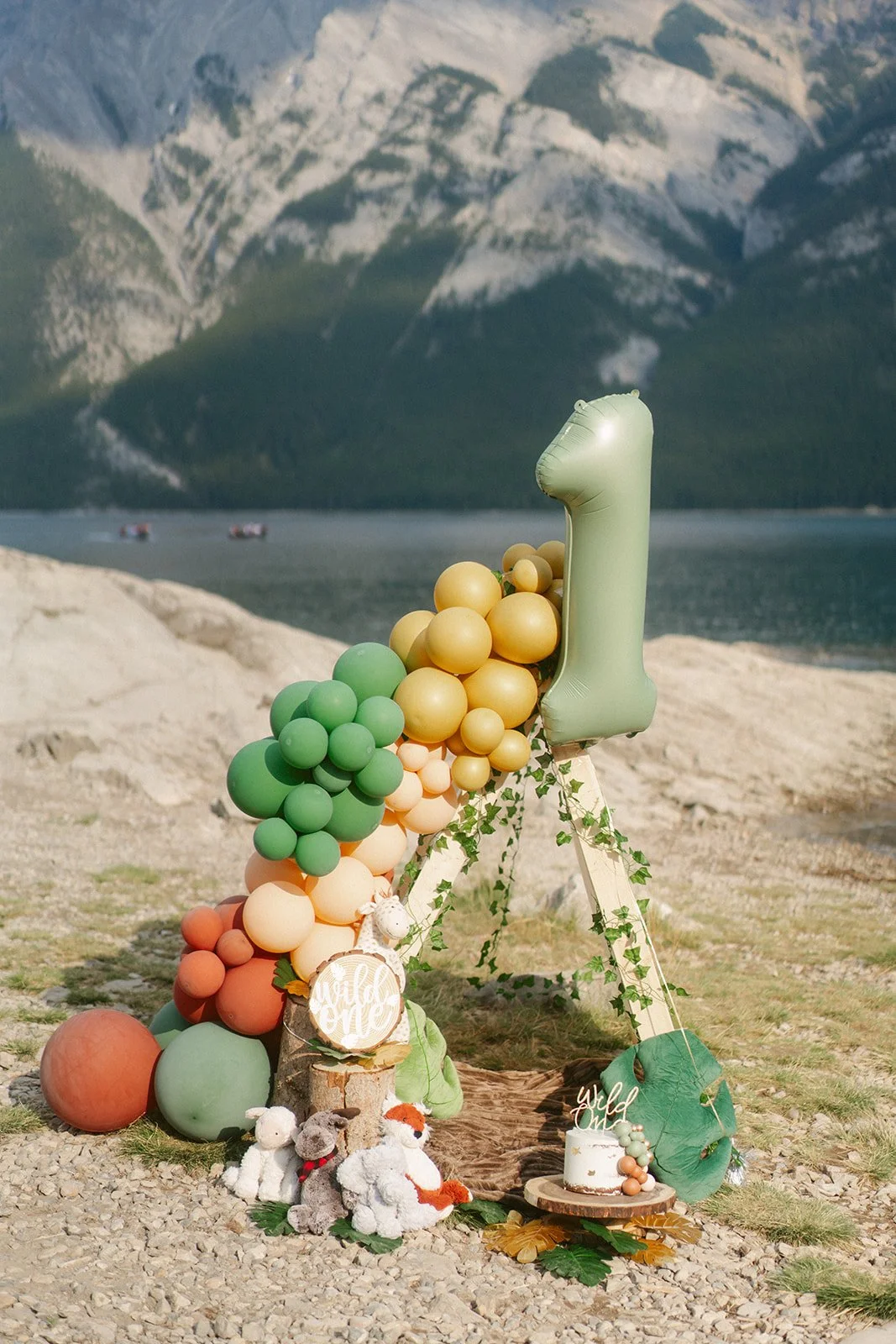Decorative arrangement with balloons celebrating a first birthday by a lake with mountains in the background.