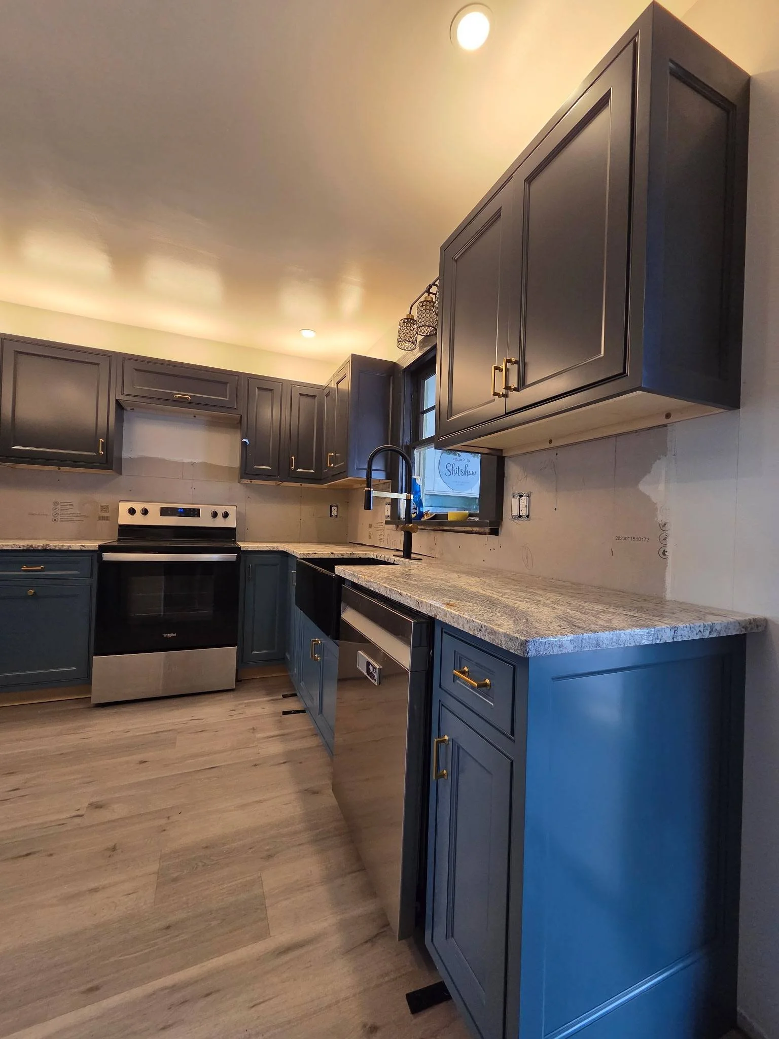 Kitchen with blue cabinets, granite countertop, stainless steel oven, dishwasher, black sink, and window with decor, under a beige ceiling with recessed lighting.
