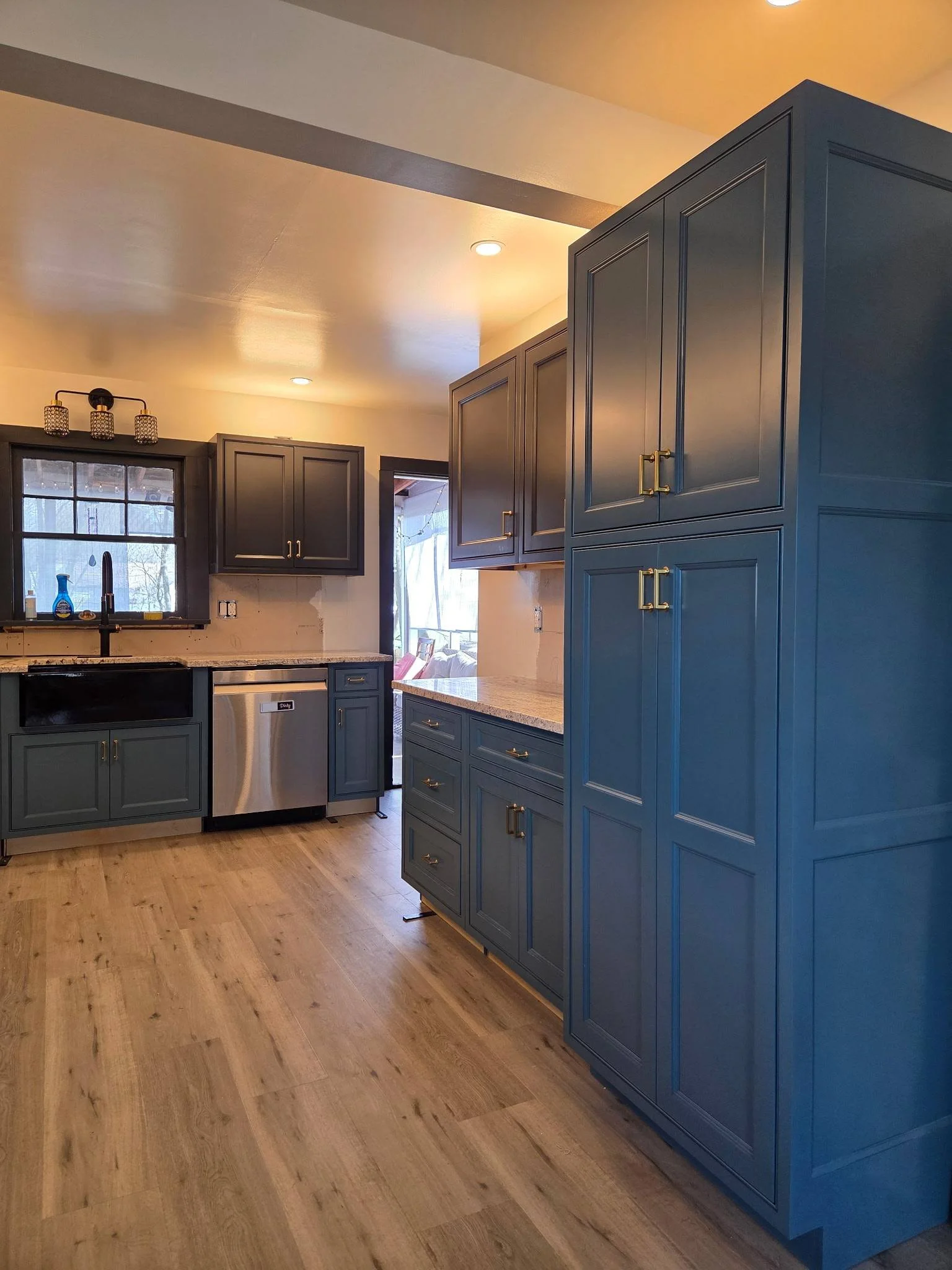 A kitchen with dark blue cabinets, a window above the sink, and wood flooring.