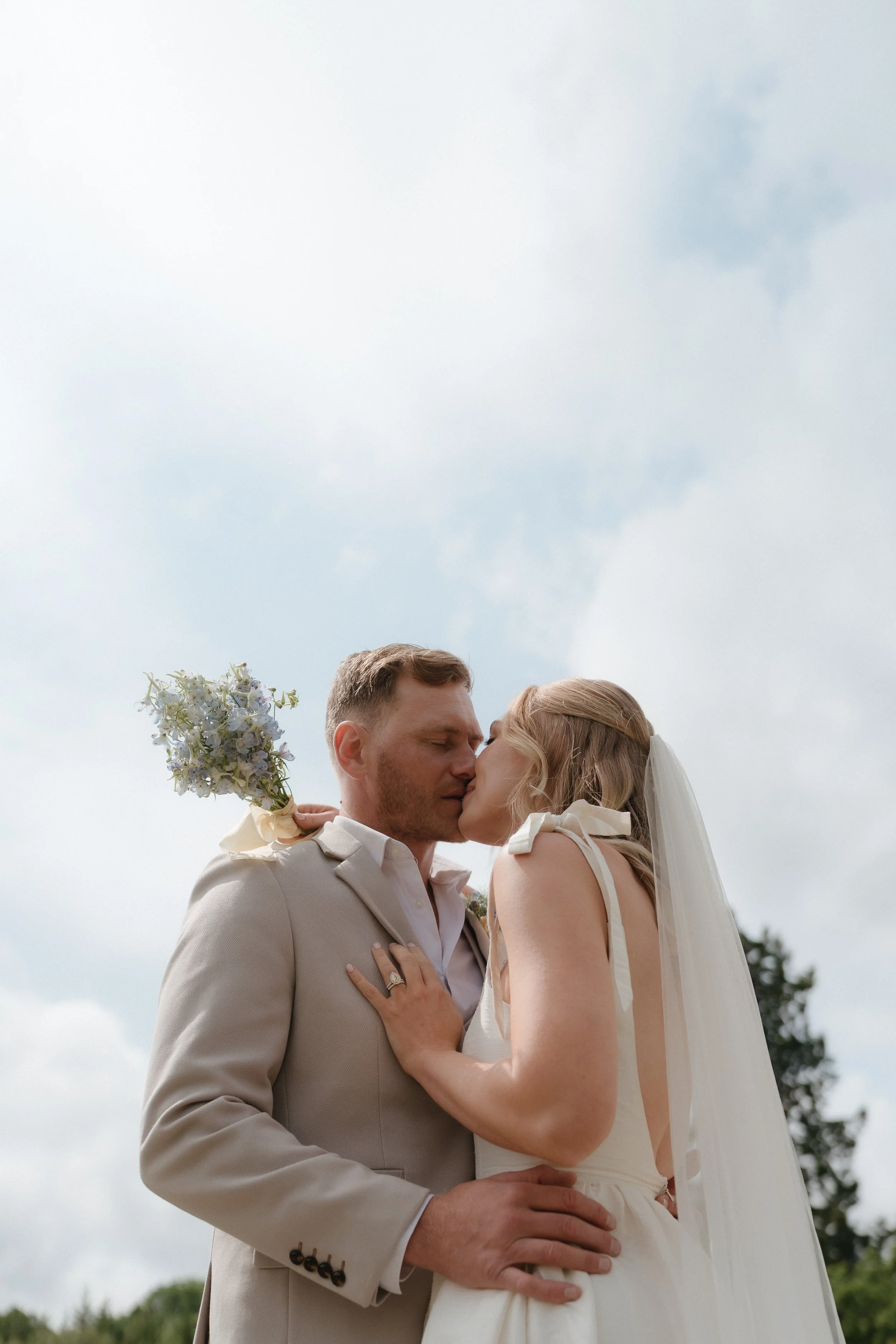 A couple dressed in wedding attire sharing a kiss outdoors against a cloudy sky at Egton Manor.