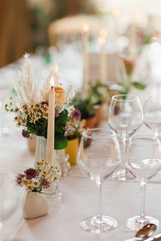 Close up of the delicate tables. Elegant glassware, white candles and sweet bud vases and potted plants