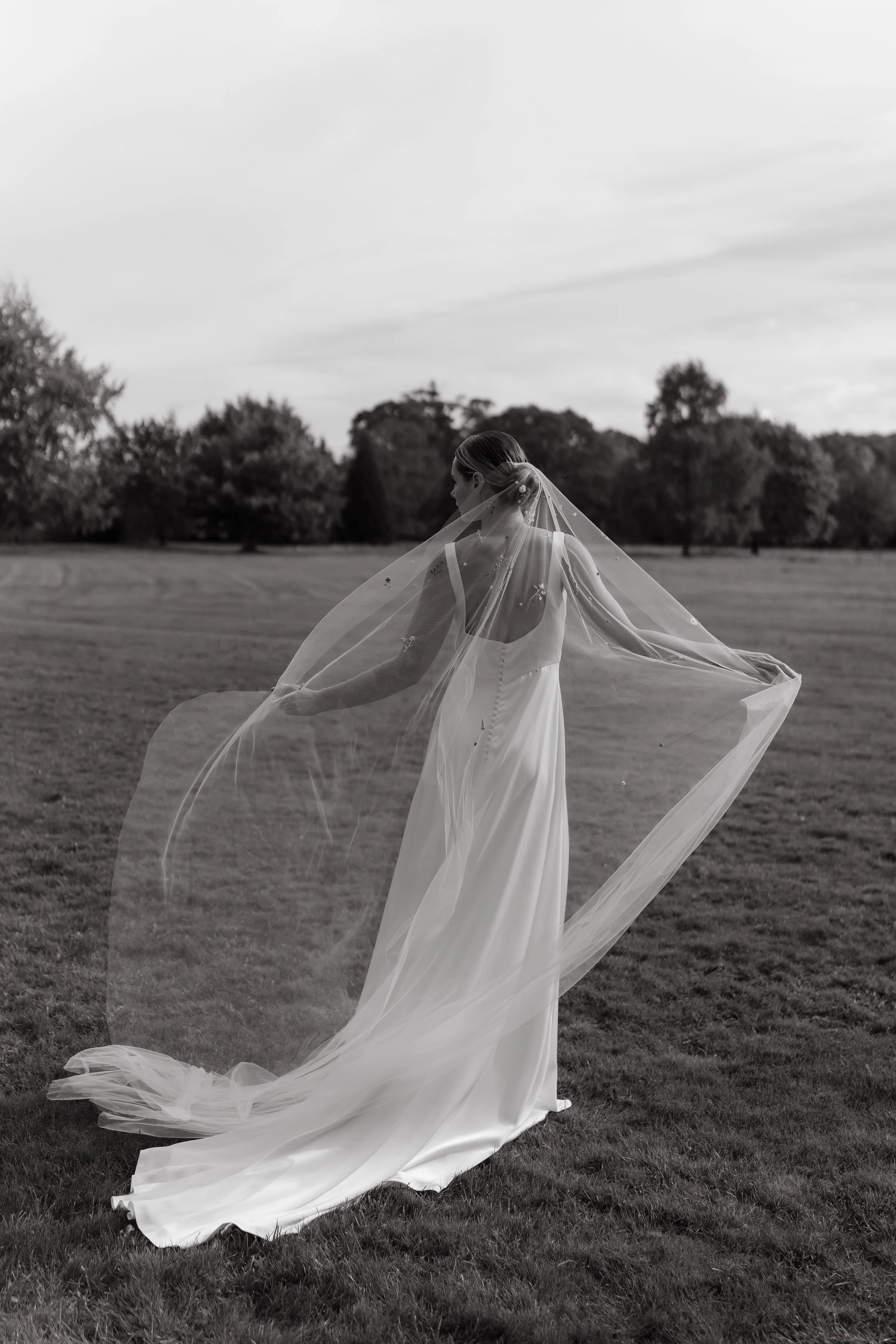 A hand-embroidered wedding veil blows in the wind as the bride looks away. Photo in black and white