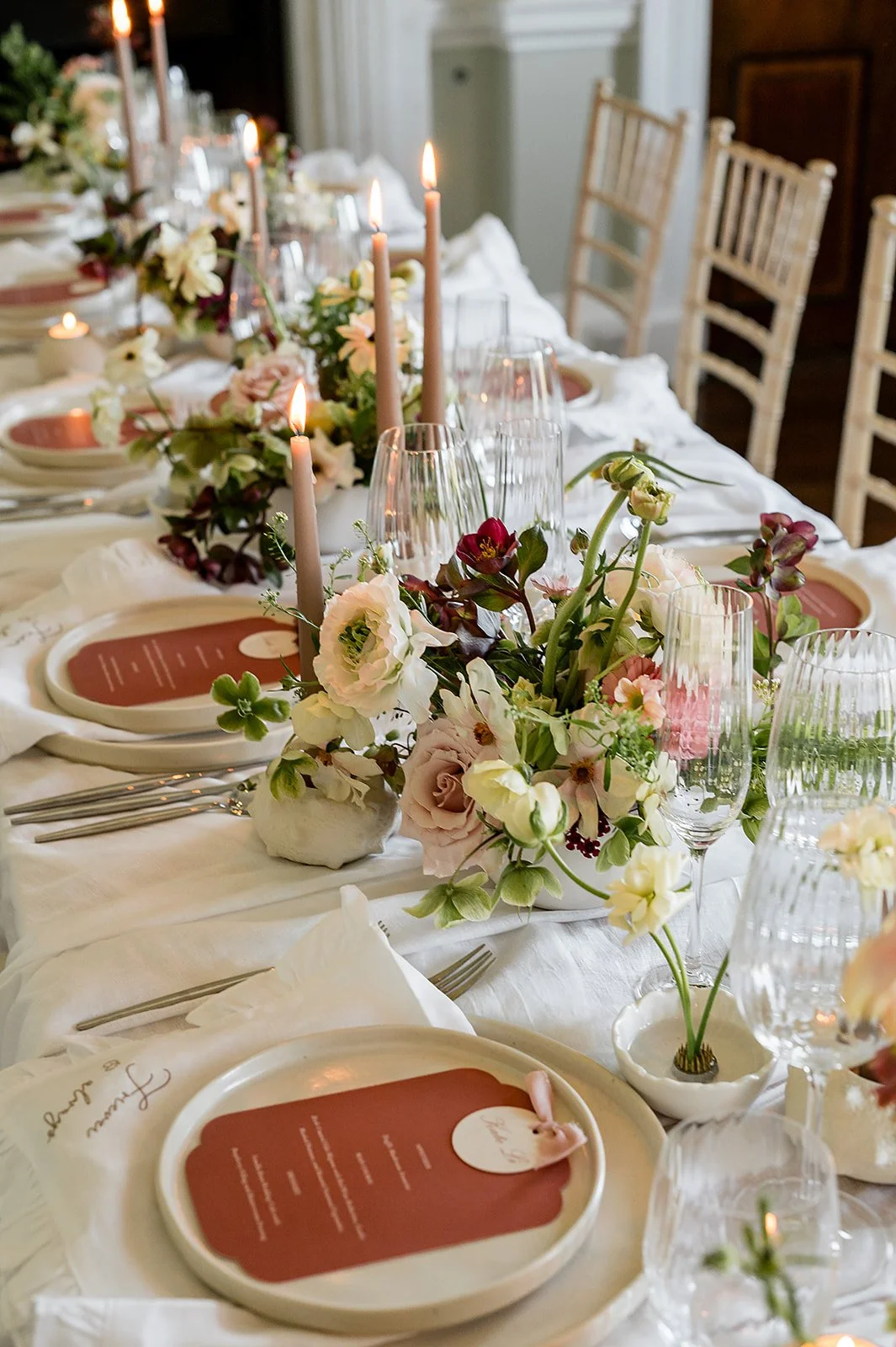 Elegant dining table decorated with floral centerpieces, pink candles, and place settings with printed menus on white plates.