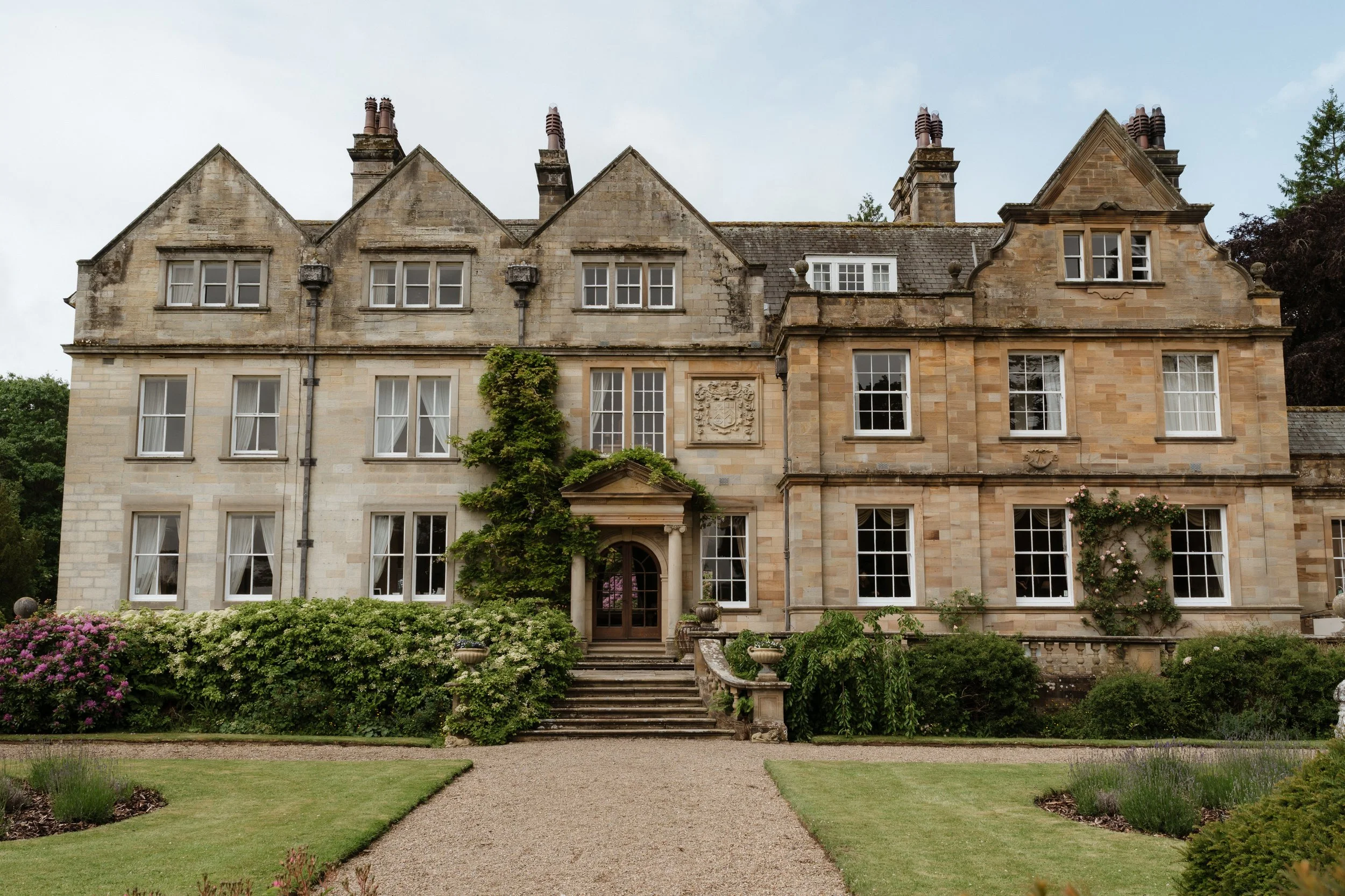 Front view of Egton Manor, a Yorkshire wedding venue, with green foliage growing up the front and stairs down onto a manicured lawn.