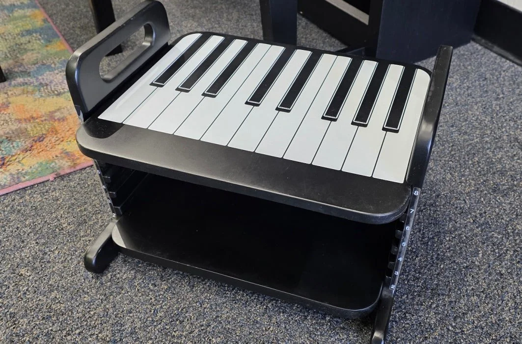 A black, adjustable piano footrest with a black and white piano key design on the top level.