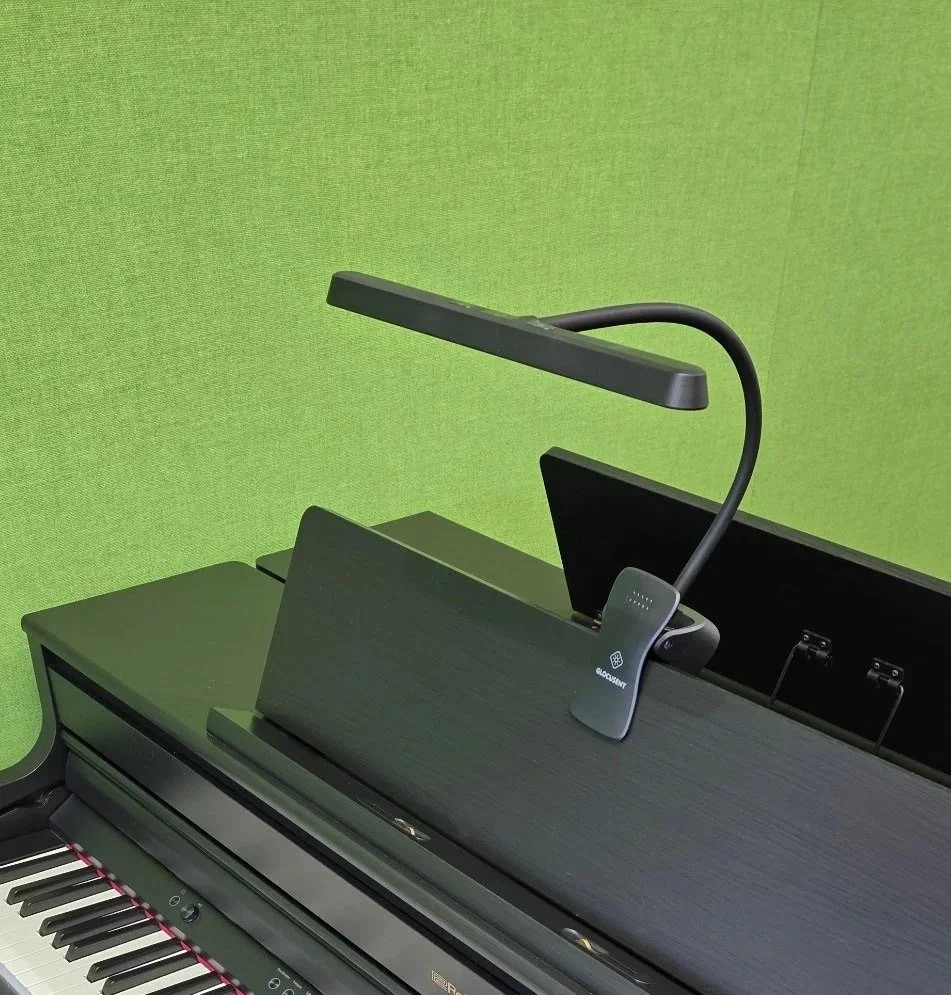 A clip-on light is attached to the music desk of a piano keyboard. It has a flexible arm for adjustment.