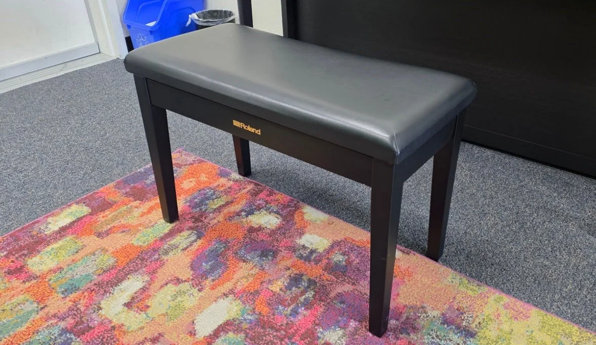 A wide, standard piano bench with padded black seating.