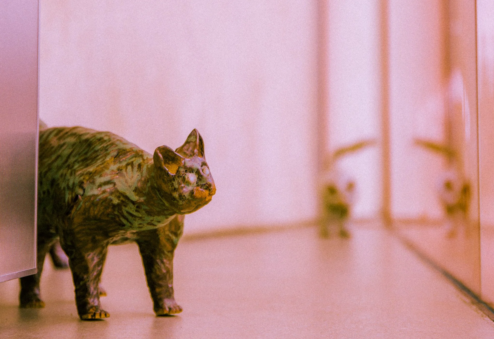 A ceramic sculpture of a dog with a textured, multicolored surface, positioned on a pinkish surface against a pink background.