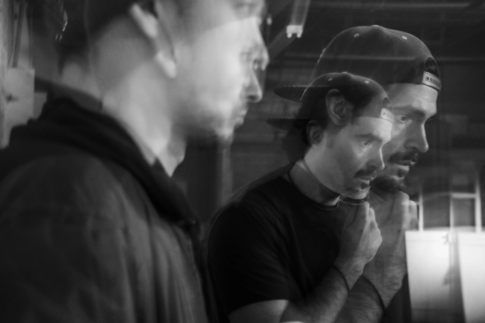Black and white photo of four people sitting side by side, each wearing hats and looking solemn or pensive.