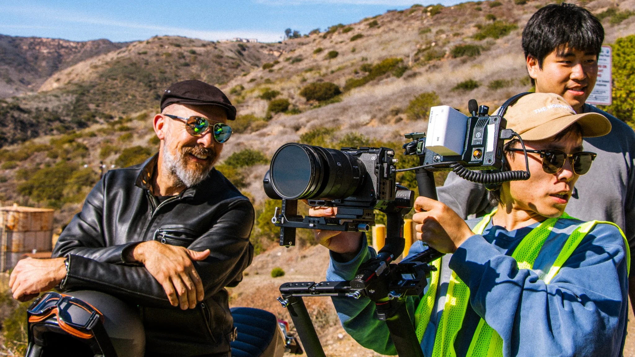 A man, a woman, and two children operating professional video filming equipment outdoors on a sunny day.