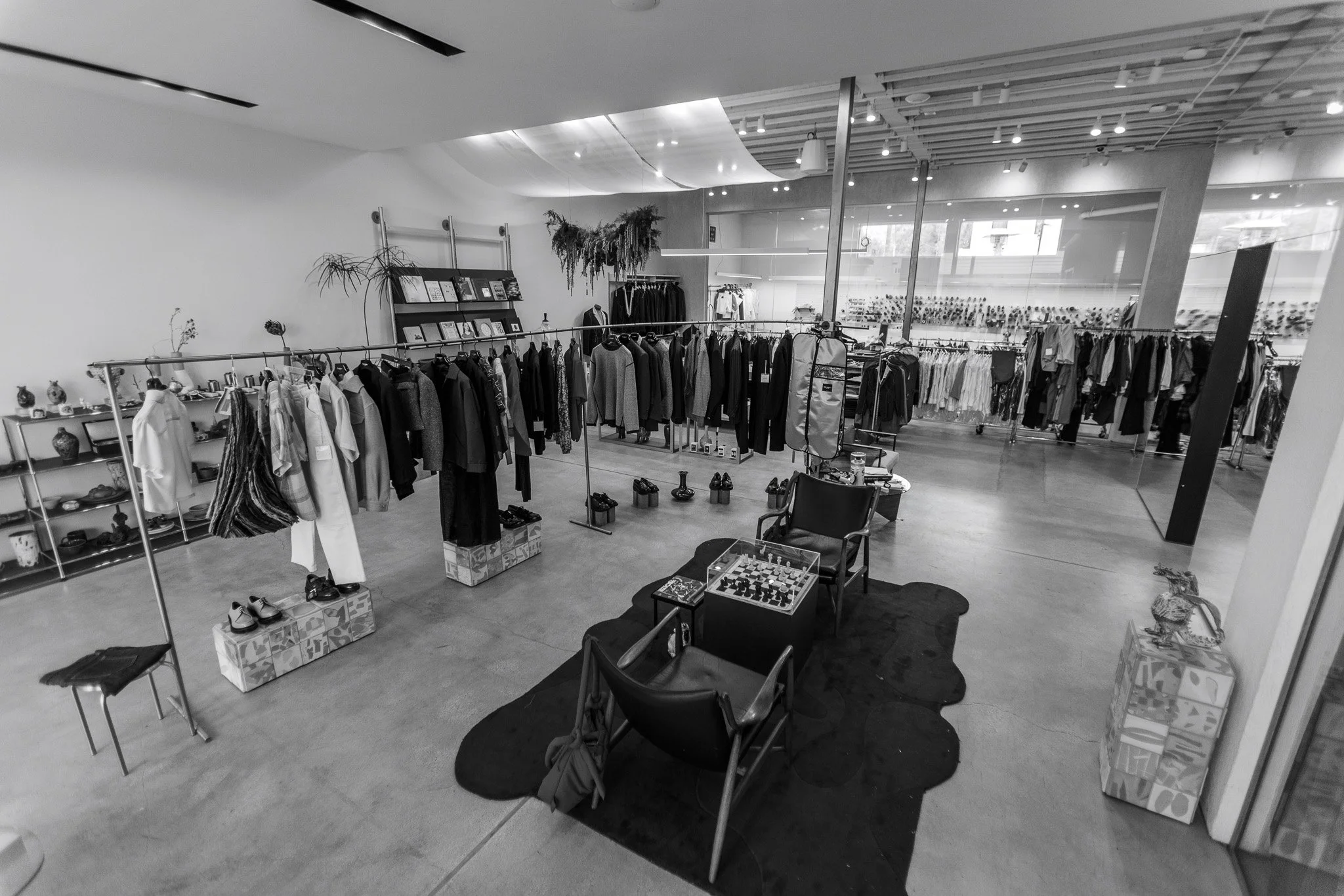 A clothing store with racks of clothes, shelves with decorative items, and a seating area with chess set and chairs.