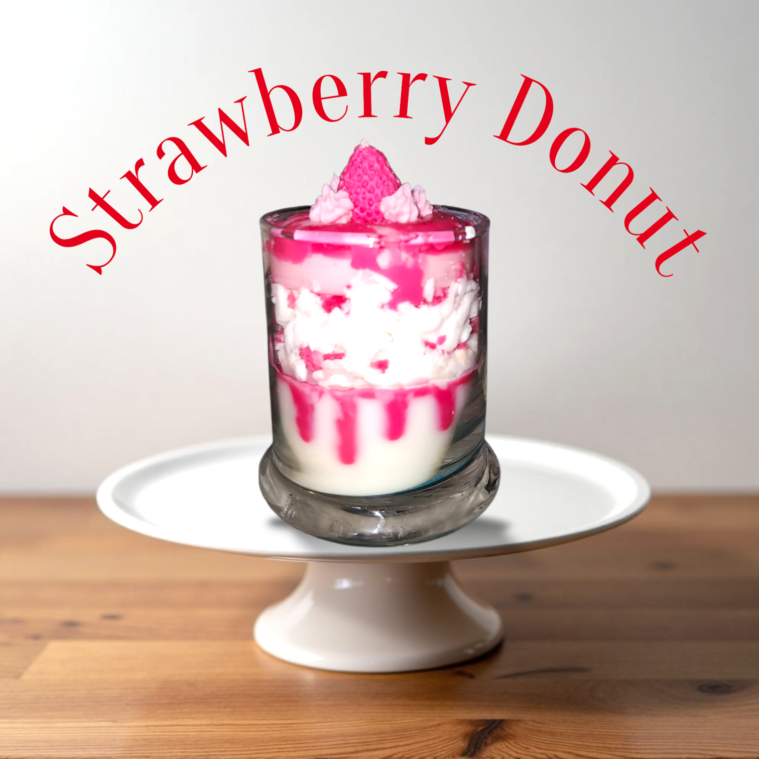 A Dessert Candle containing a layered strawberry sundae with pink syrup, whipped cream, and a strawberry top, placed on a white cake stand on a wooden surface.