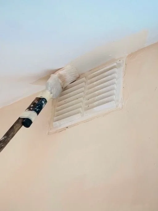 A close-up of a paintbrush with white paint dripping off it, above a paint can, suggesting that the brush has just been dipped and is ready for use.