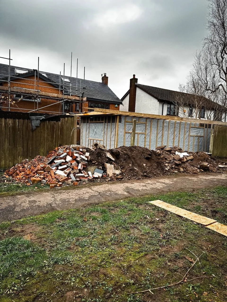 A construction site with a large pile of bricks and dirt in front of a residential building with scaffolding.