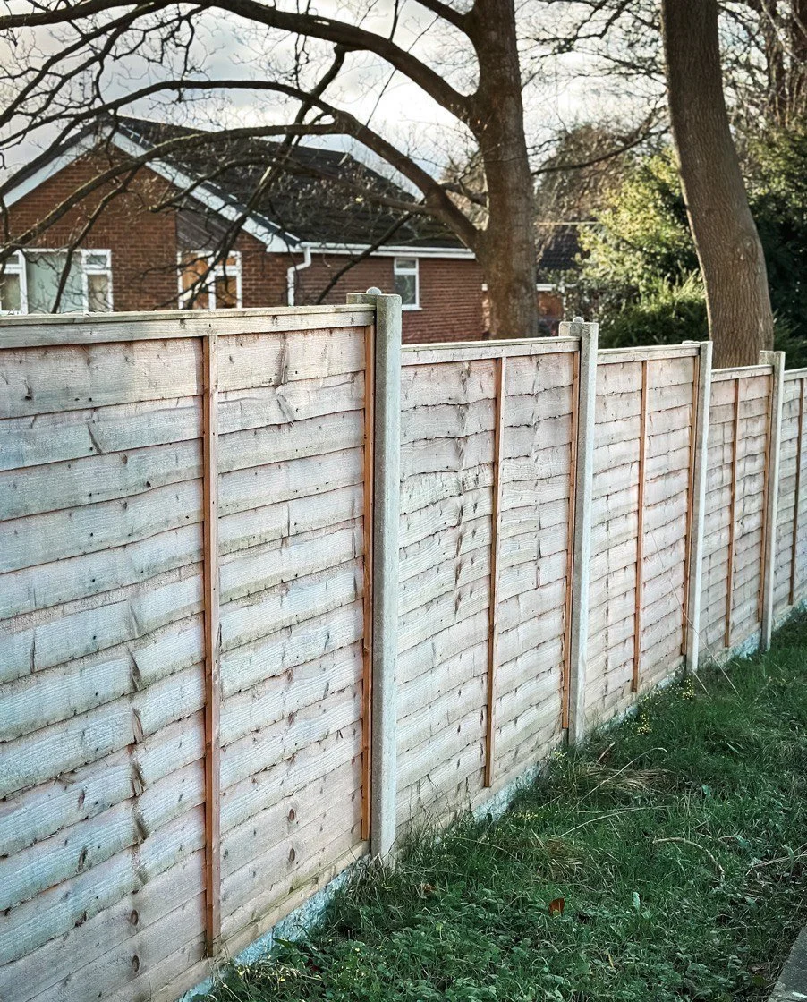 Fencing on green grass next to a brown house and a tree
