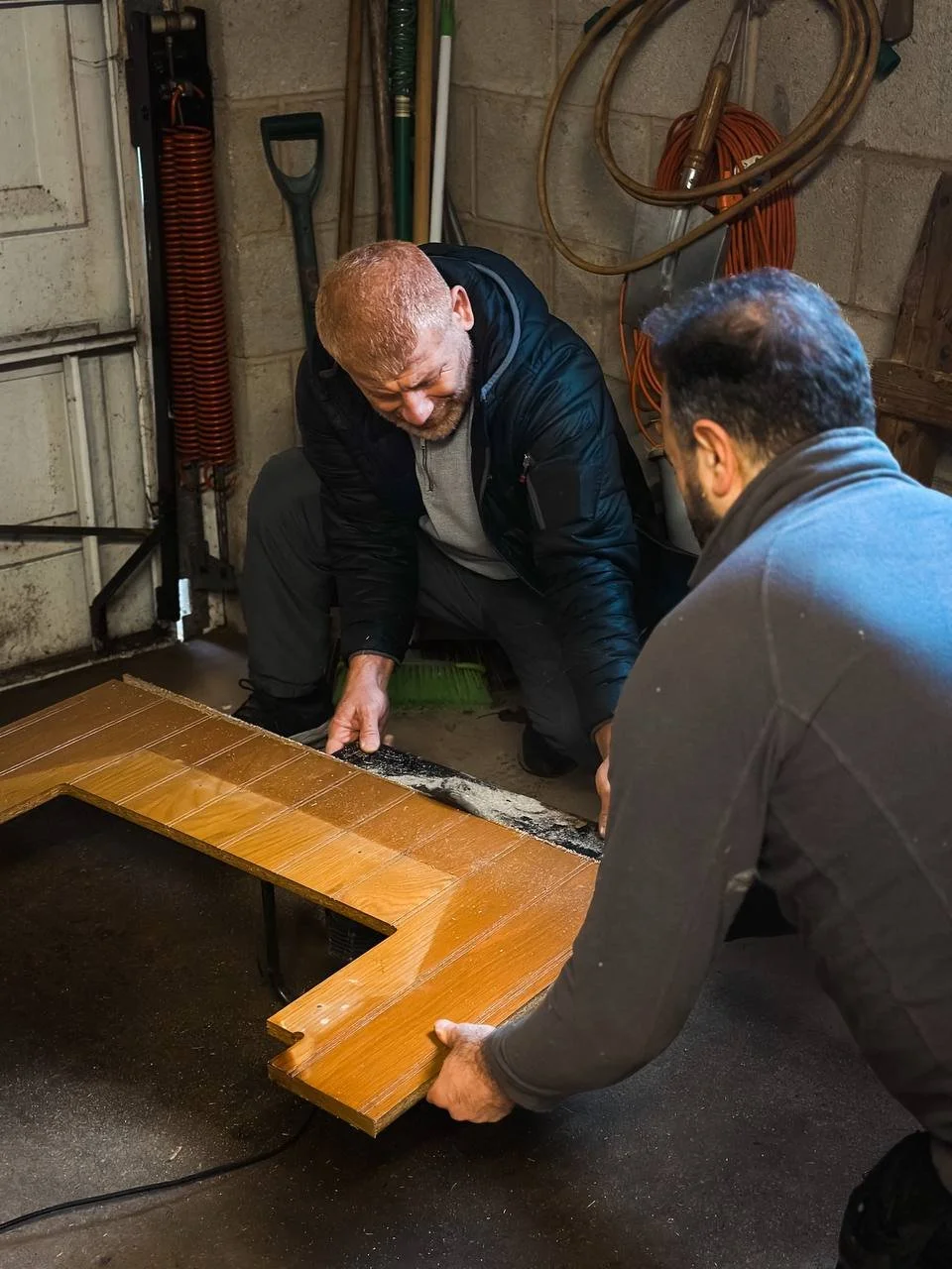 Two men examining or working on a wooden staircase component in a workshop setting.