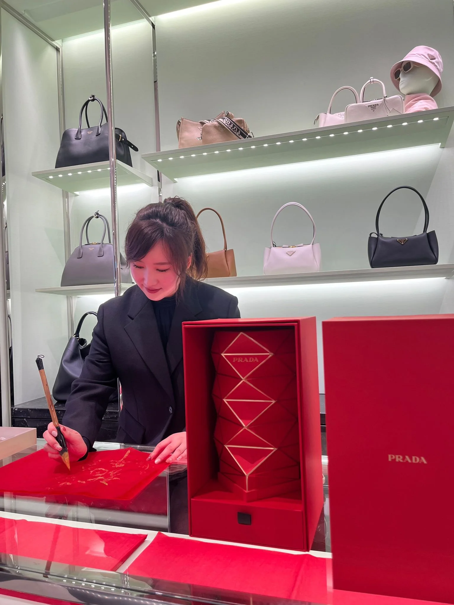 Brand event: Artist is writing on a red surface; a red Prada gift box is visible Artist: Yi Ling Lai, the founder of lingsspace.