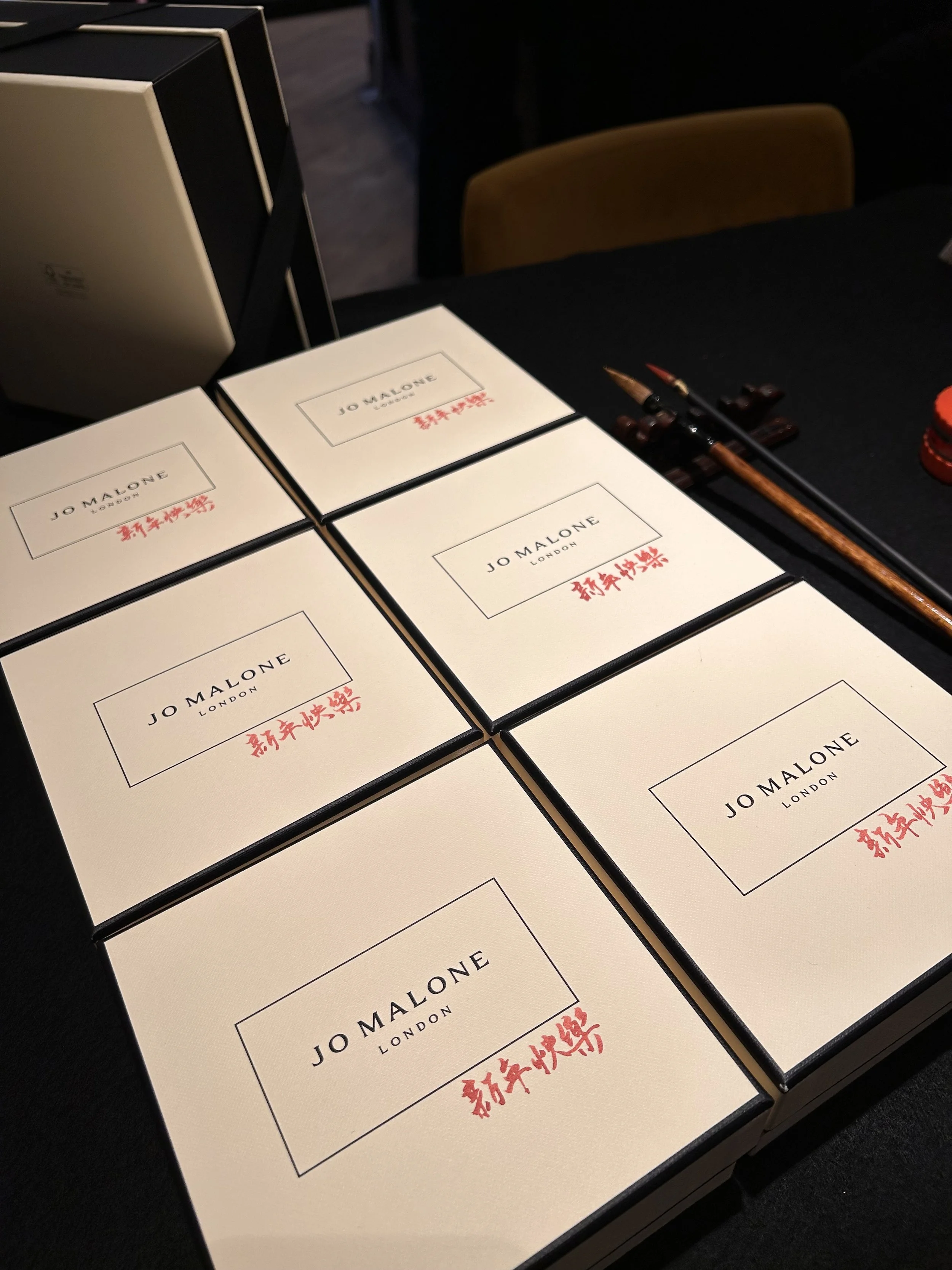 Six Jo Malone London boxes with black edges and red Chinese characters on a table, alongside writing brushes. Design by Yi Ling Lai, the founder of lingsspace