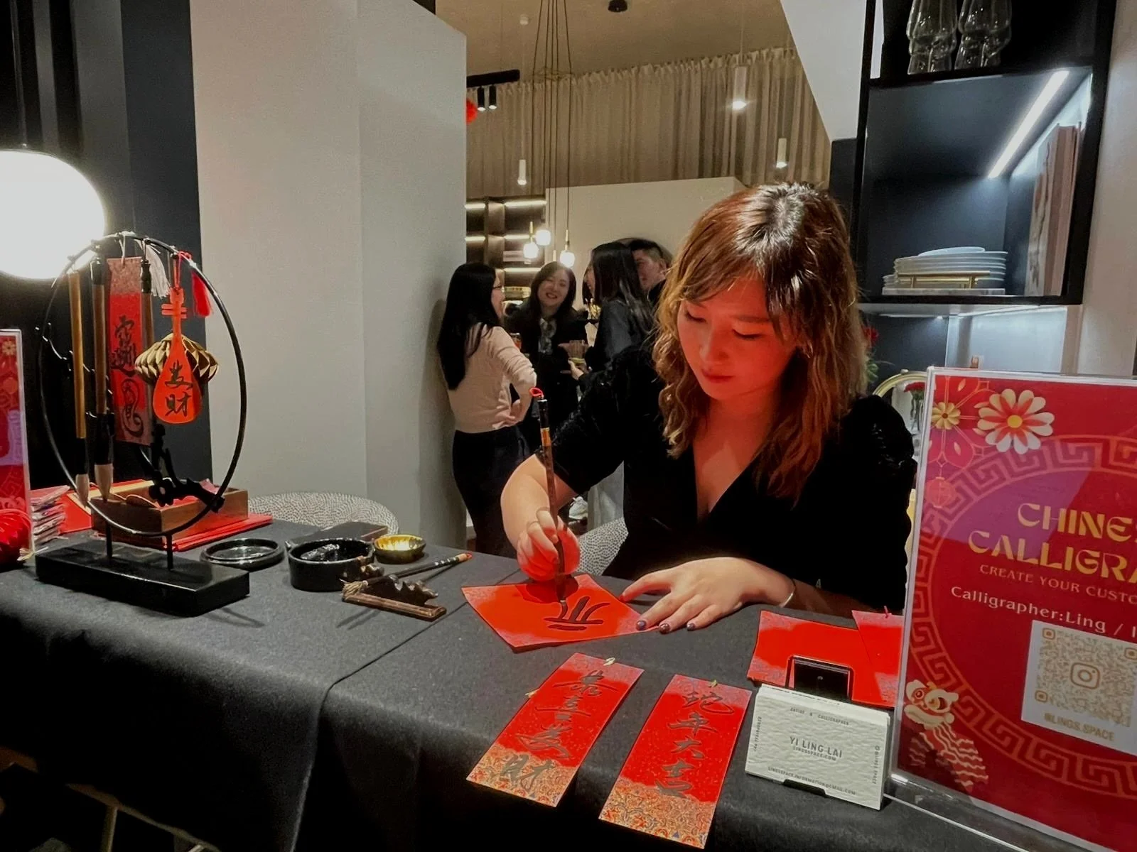 Company event: Woman practicing Chinese calligraphy at a table with decorative items and artwork. Artist: Yi Ling Lai, the founder of lingsspace