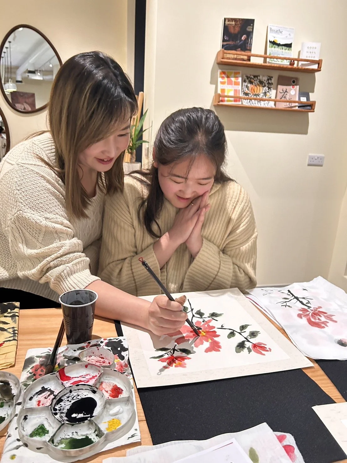 Weekend Chinese painting workshop: Two people engaged in Chinese painting, using brushes and a palette of colors, creating floral art on paper at a wooden table. workshop teacher: Yi Ling Lai, the founder of lingsspace