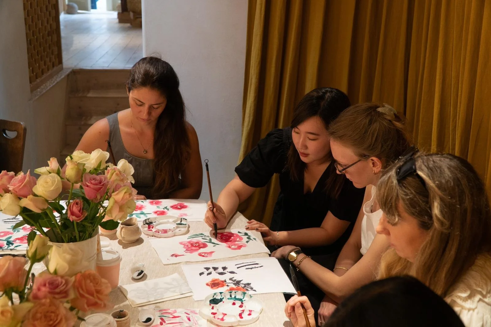 Workshop: A group of women participating in an art workshop, painting floral designs on paper. A vase of roses is on the table. Workshop teacher: Yi Ling Lai, the founder of lingsspace. Location: Fern. London
