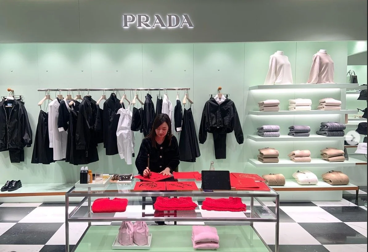 Brand Event: Prada store interior with woman working, clothing on display, and shelves of folded garments. Artist: Yi Ling Lai, the founder of lingsspace