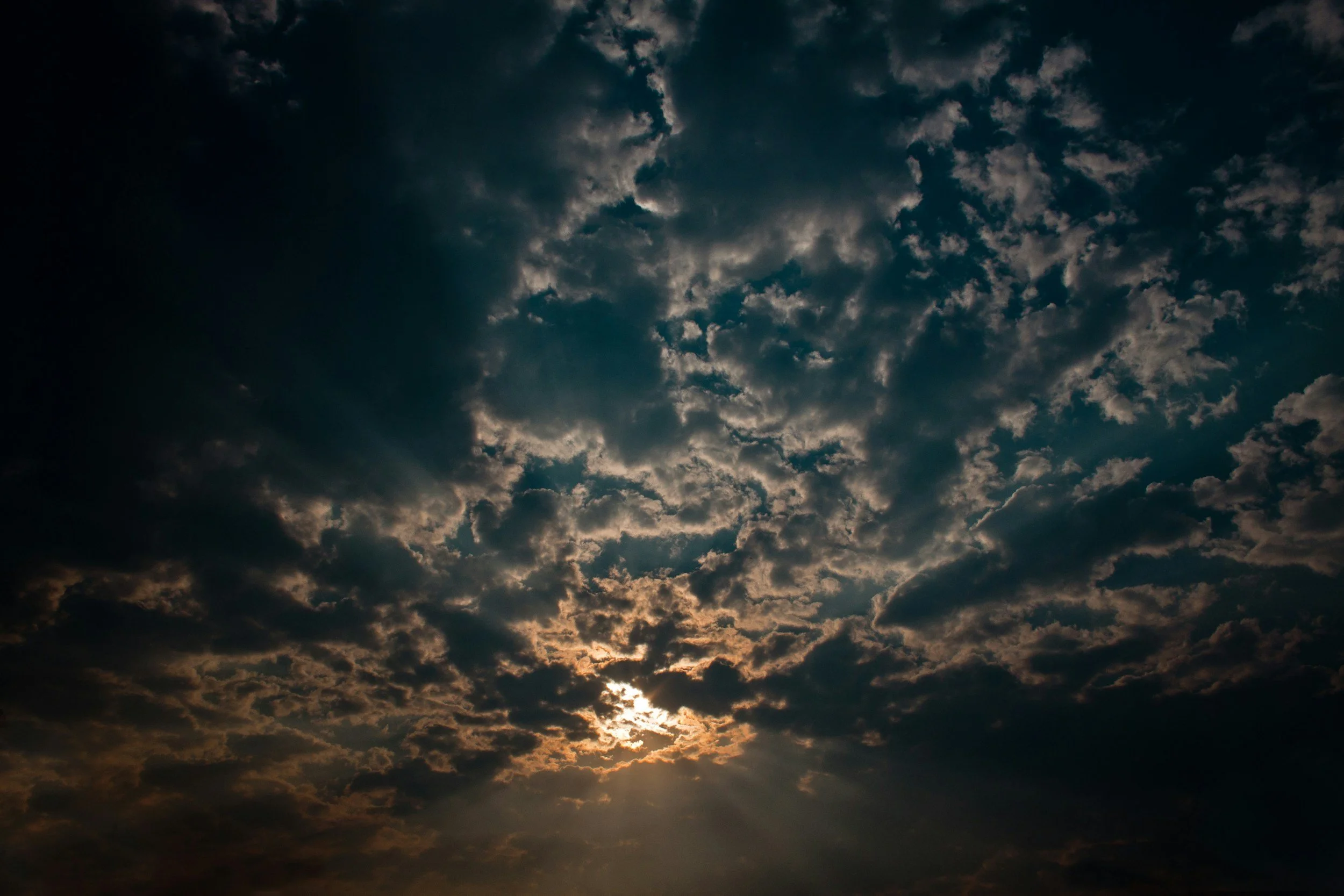 Dark cloudy sky with the sun partially visible, creating rays and a glow around the clouds.