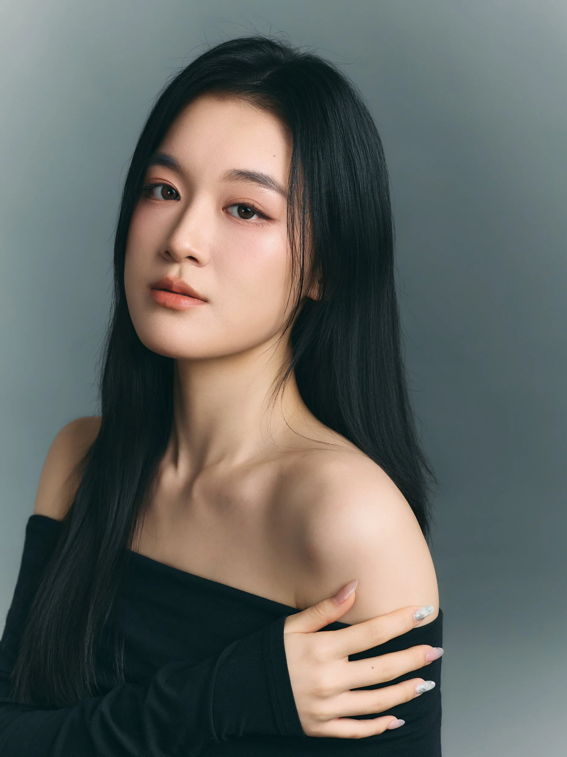Studio portrait of a woman in an off-shoulder black top with her arm across her chest