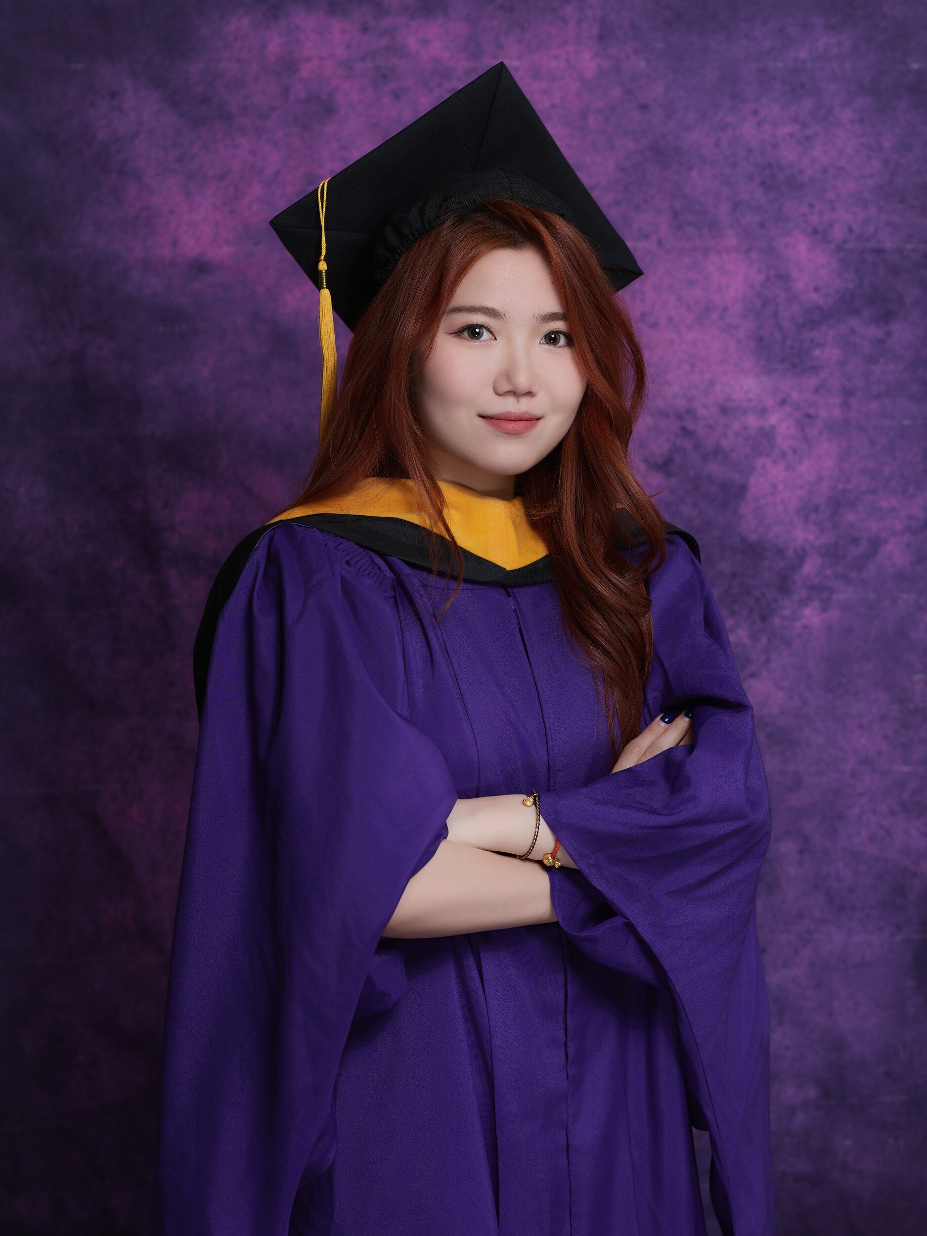 Graduate with auburn hair in cap, arms crossed