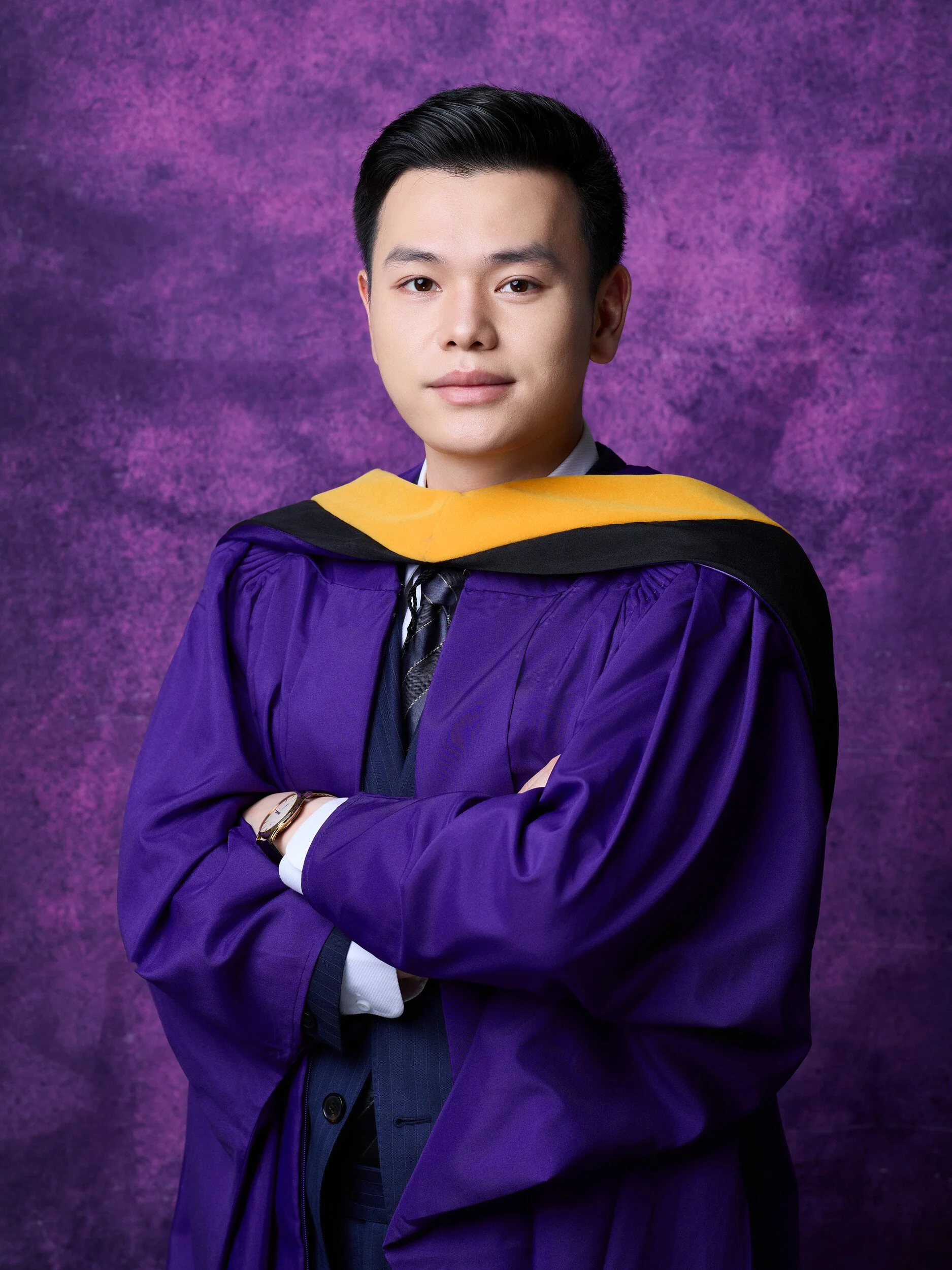 NYU graduation portrait of a young man in a suit under a purple gown with a gold hood
