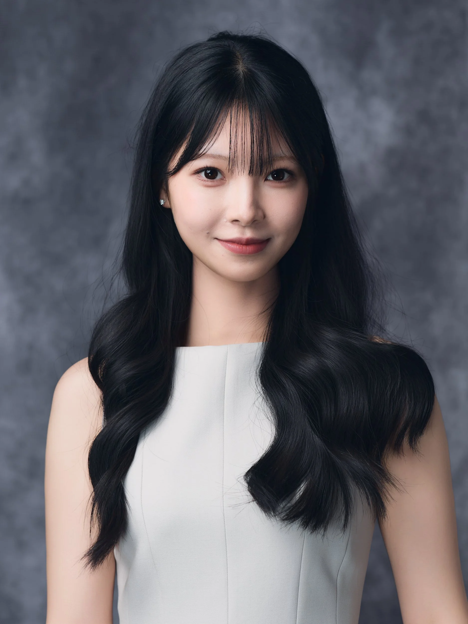 Headshot of a smiling woman with long dark hair on a grey textured backdrop