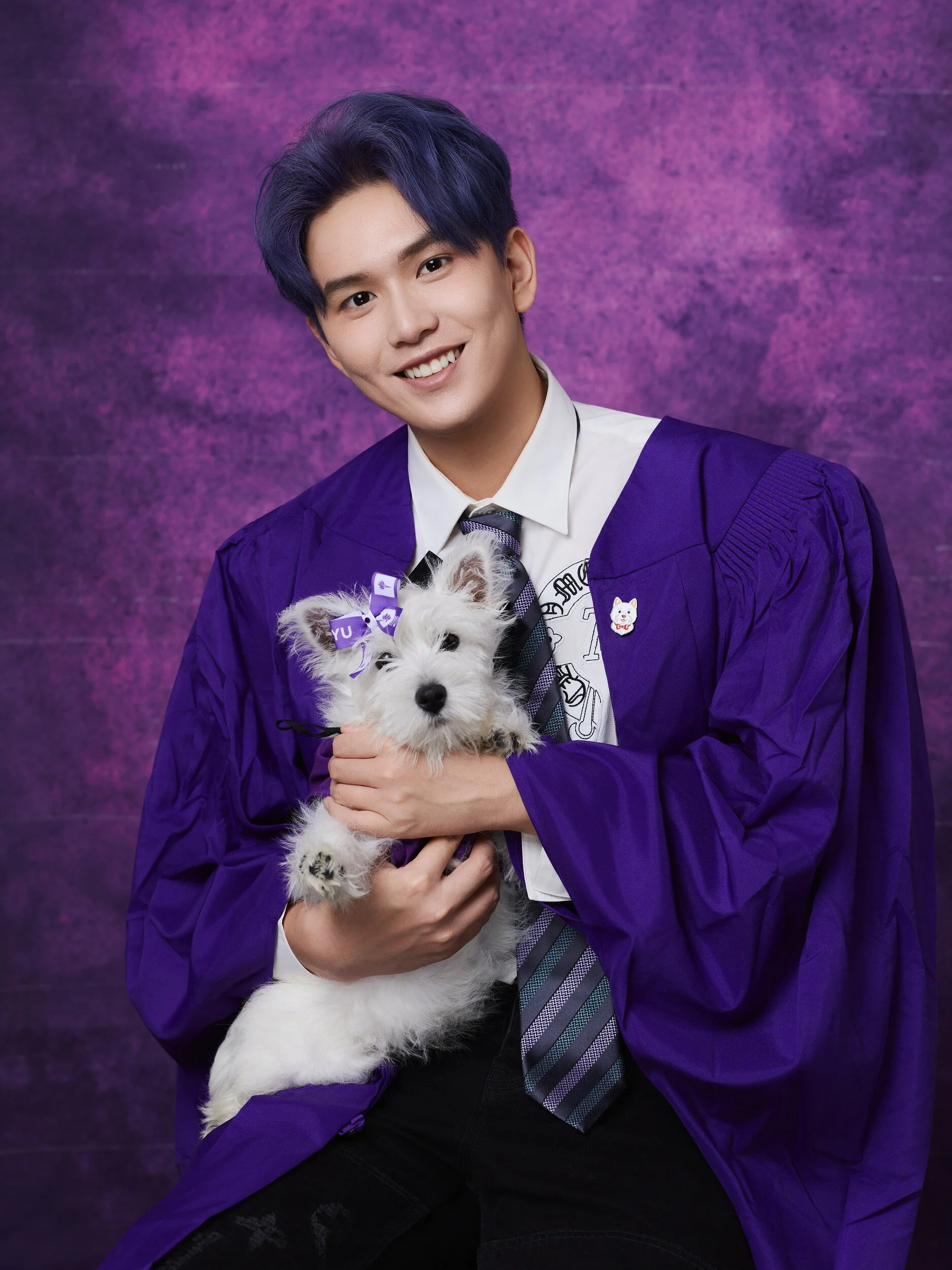 NYU graduation portrait of a young man with purple hair holding a white terrier