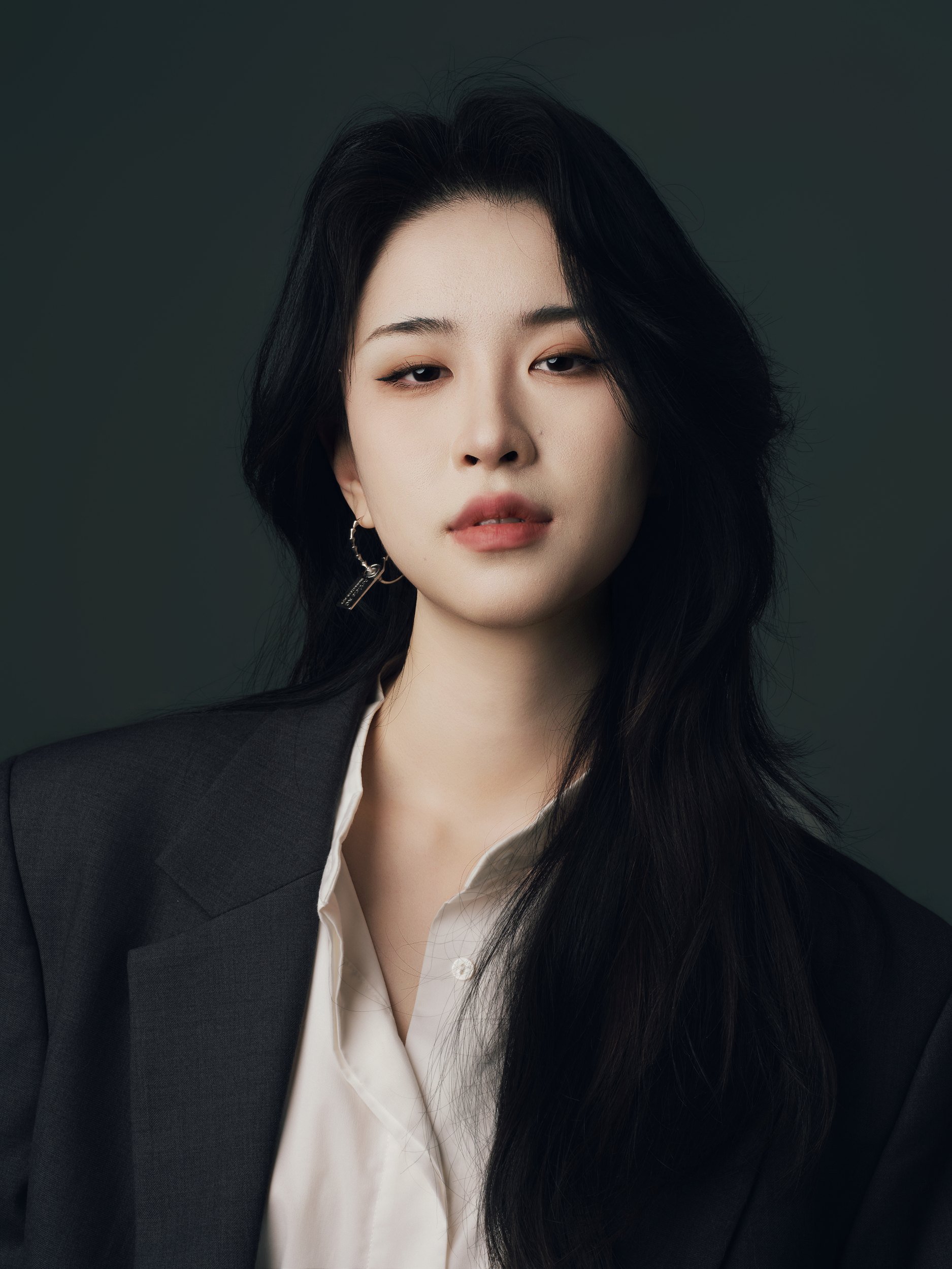 Studio portrait of a woman in a black blazer and white shirt on a dark grey backdrop