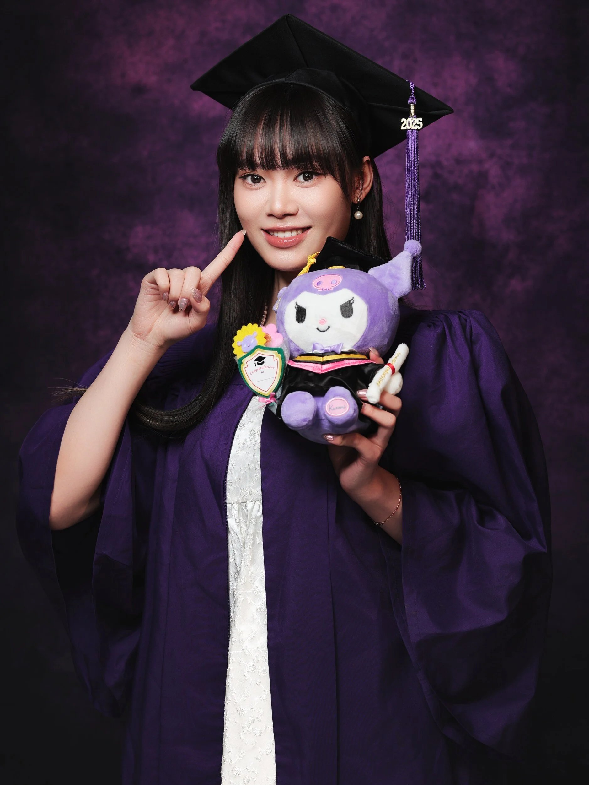 NYU graduation portrait of a woman with bangs winking and holding a Kuromi plush