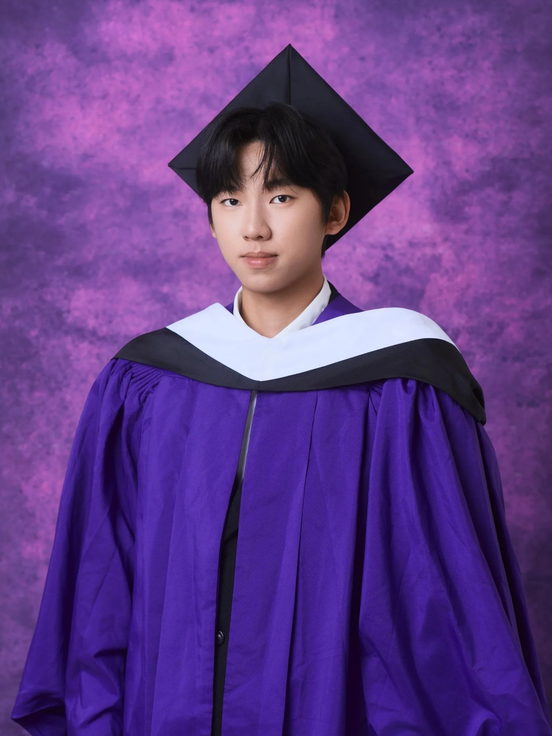 NYU graduation portrait of a young man with long hair in a purple gown and cap