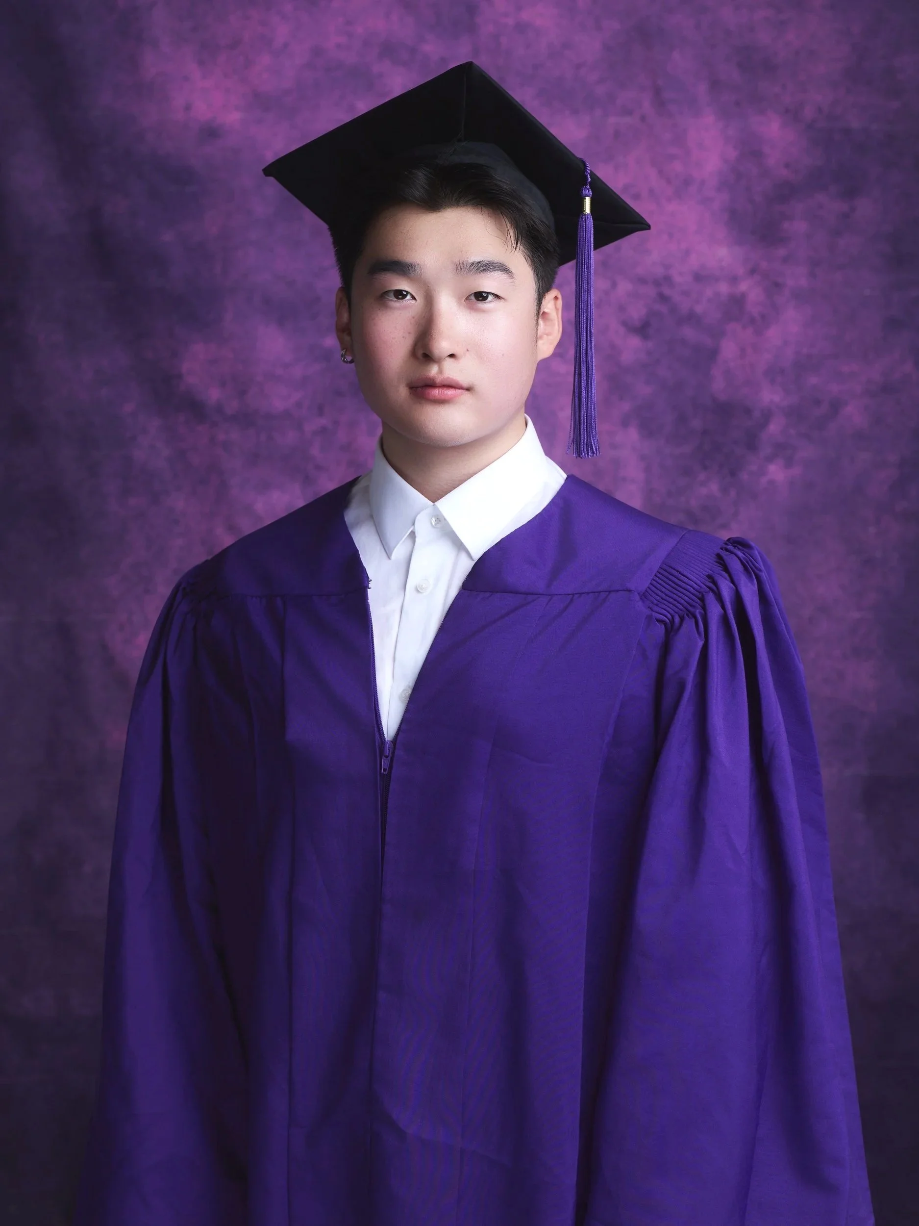 NYU graduation portrait of a man in a purple gown and cap