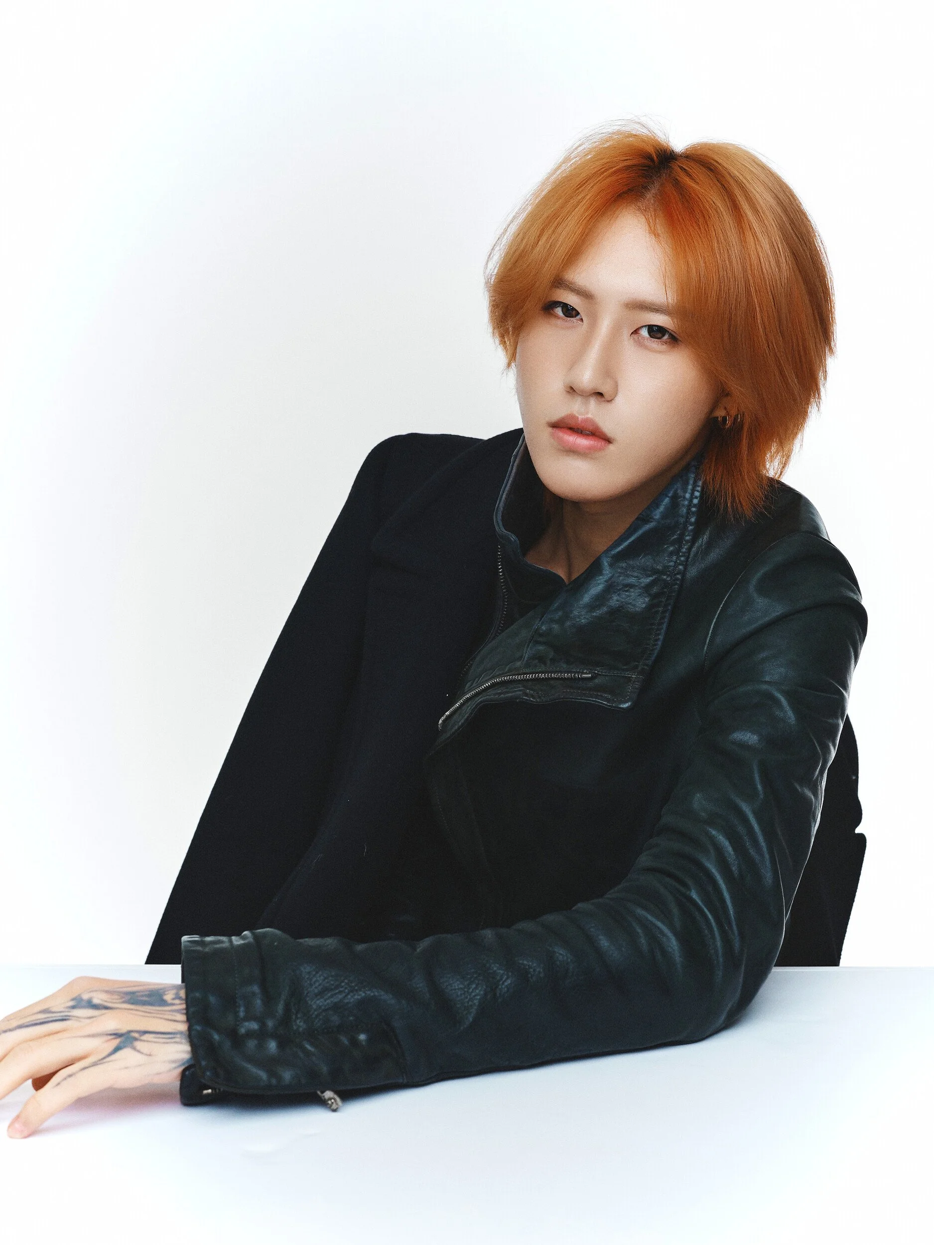 Studio portrait of a man with orange hair leaning on a table