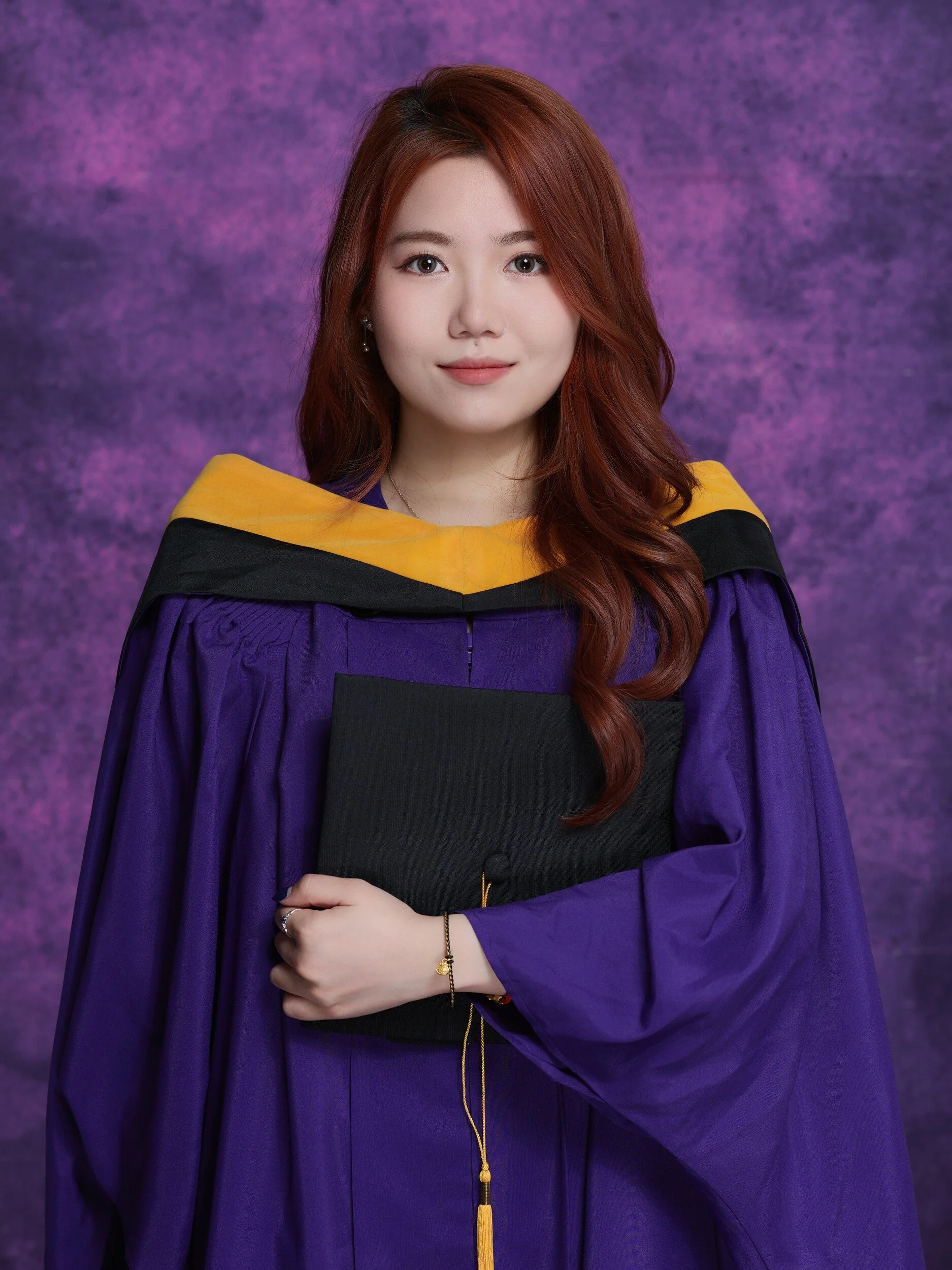 Graduate with auburn hair holding a diploma cover