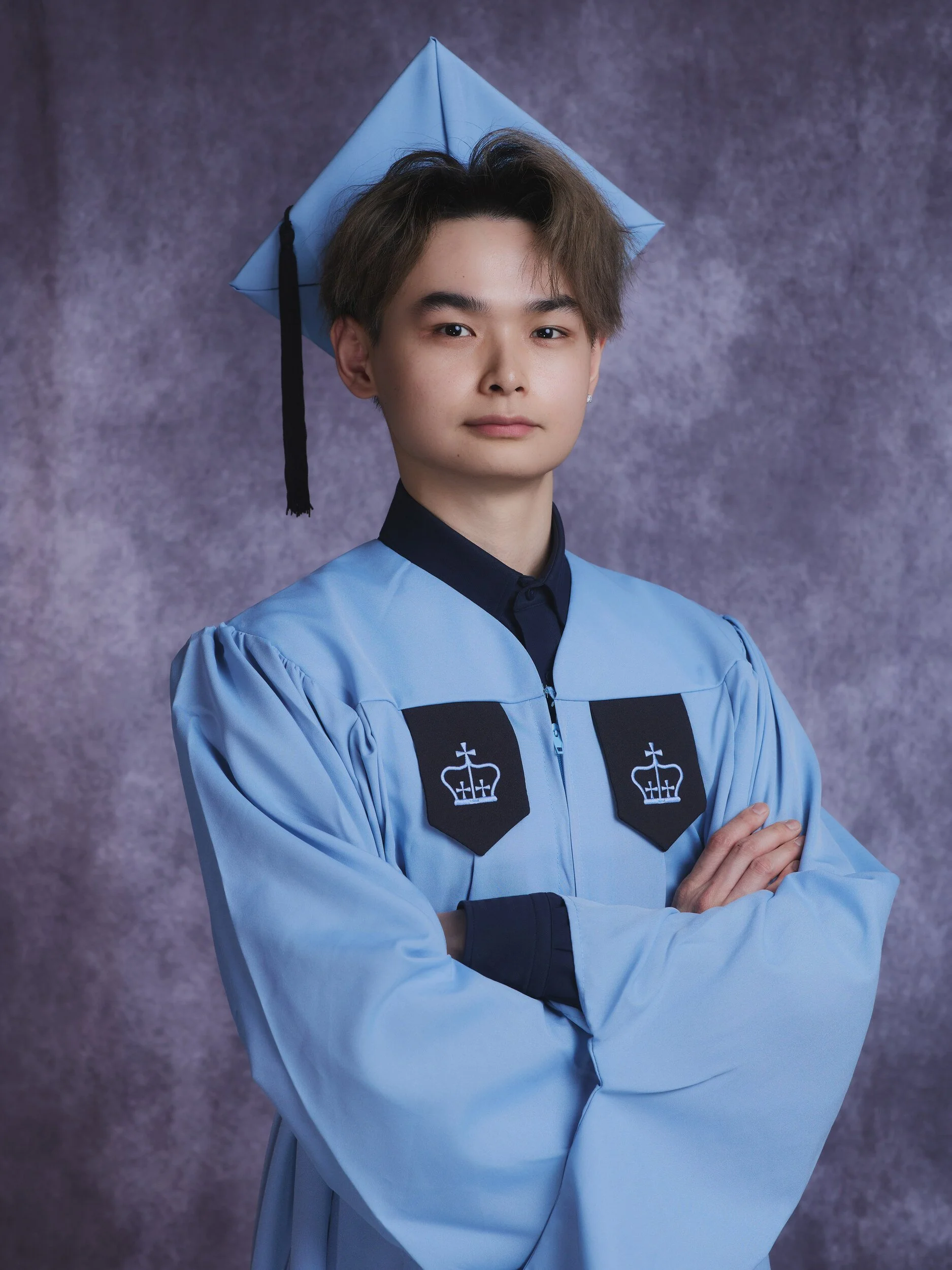Columbia graduation portrait of a young man in a light blue gown with arms crossed