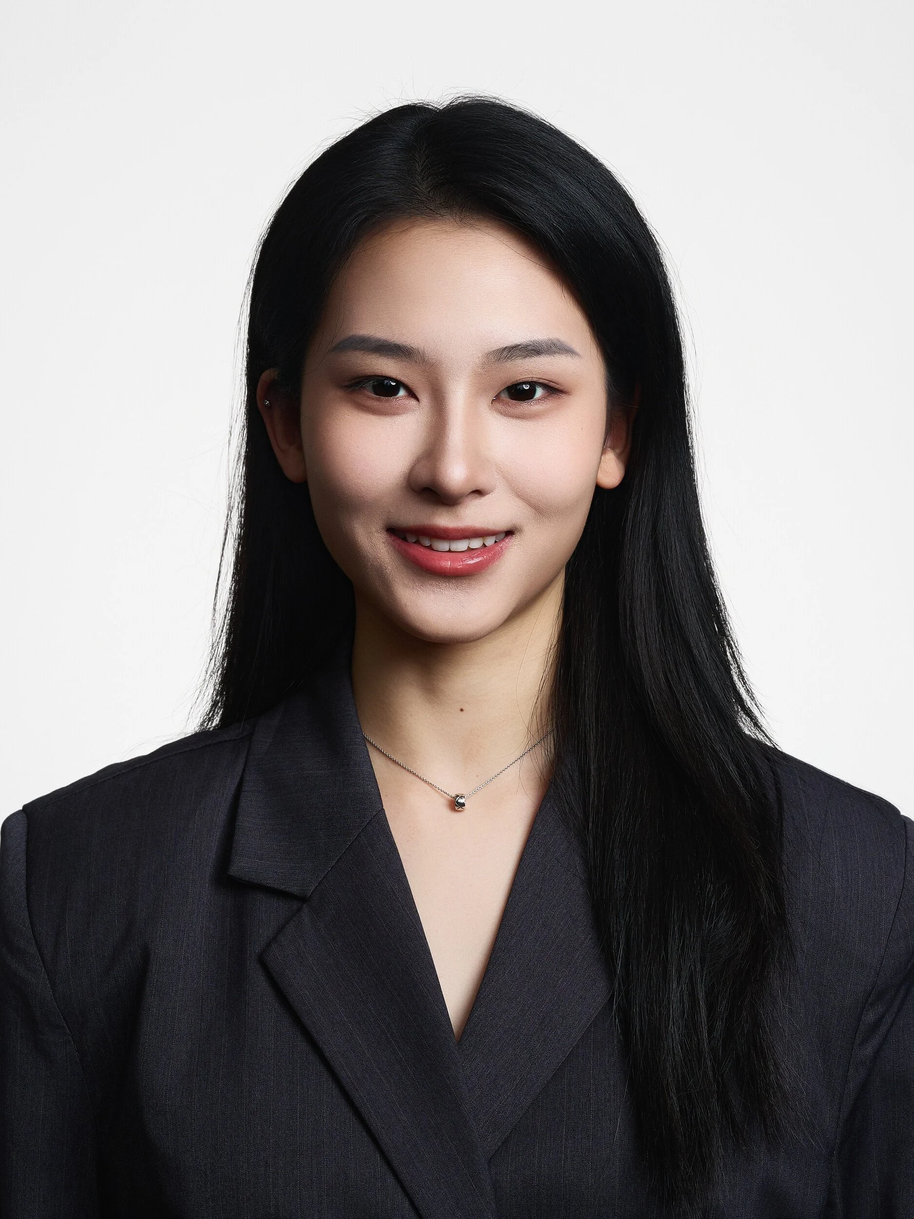 Professional headshot of a smiling woman with long black hair in a dark blazer on white